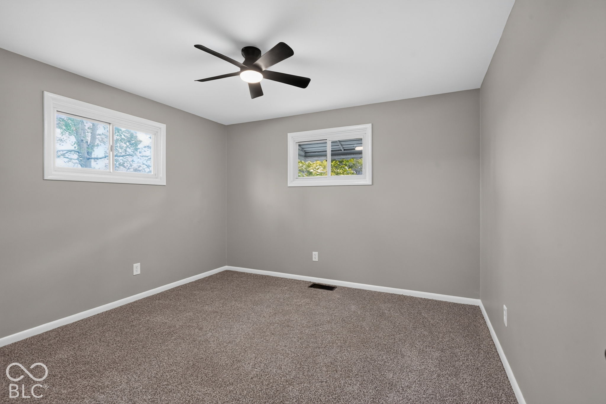 Neutral-toned interior space featuring wall-to-wall carpeting, two sliding windows, and a ceiling fan with integrated lighting