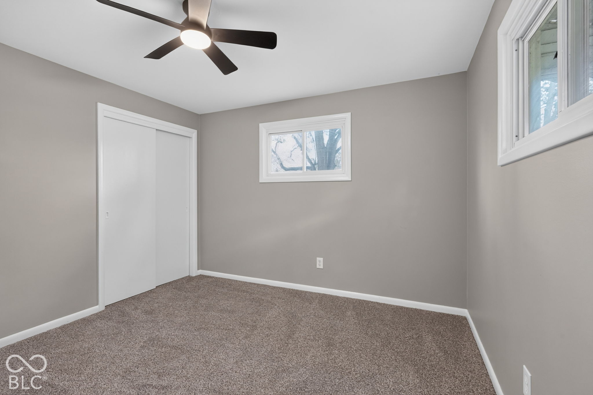 Room featuring neutral wall tones, carpeted flooring, sliding closet doors, a multi-blade ceiling fan with integrated lighting, and dual white-framed windows