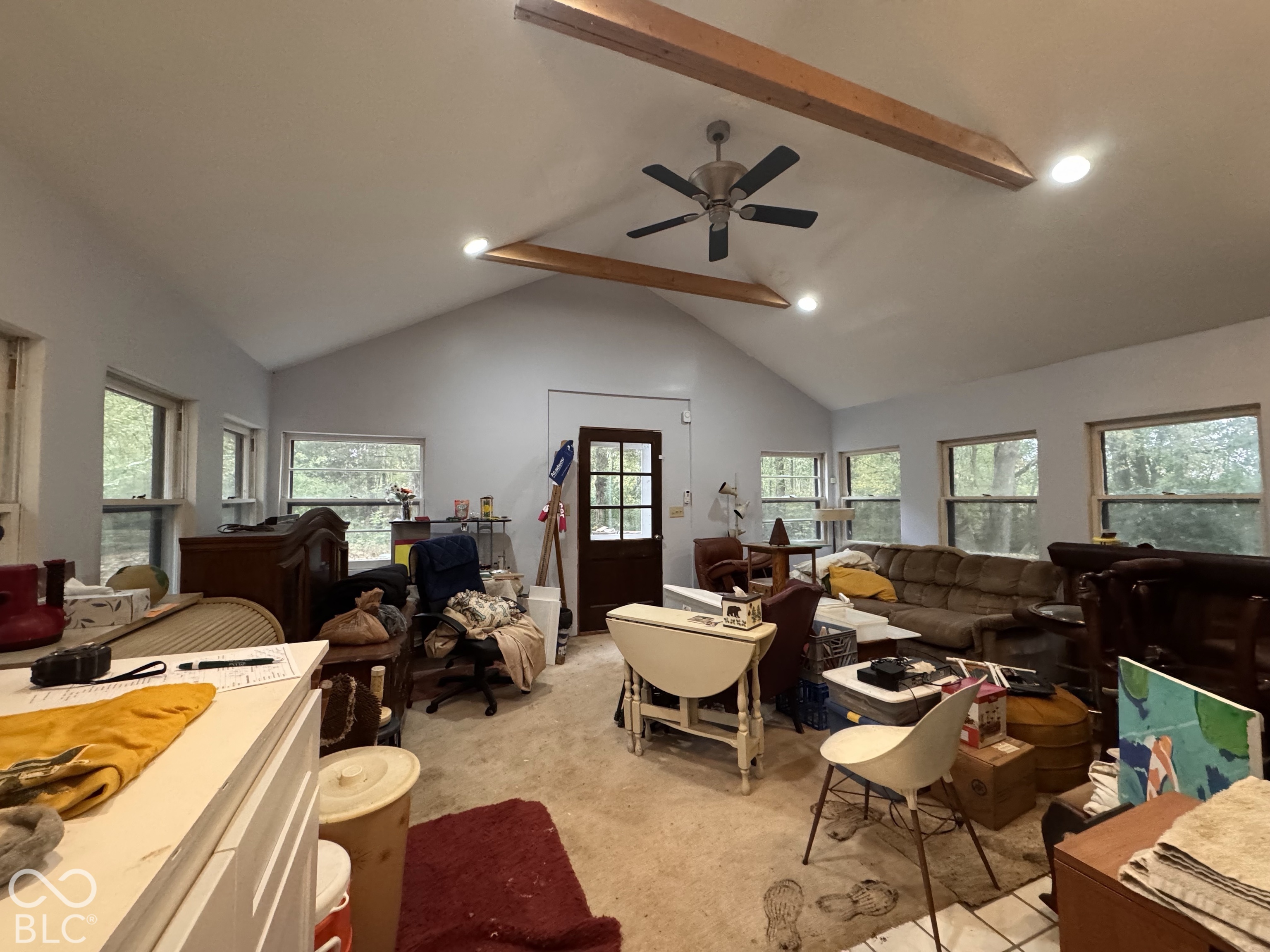 Vaulted ceiling featuring exposed wood-tone beams, recessed lighting, and a multi-blade ceiling fan, accented by multiple windows and a solid-panel entry door