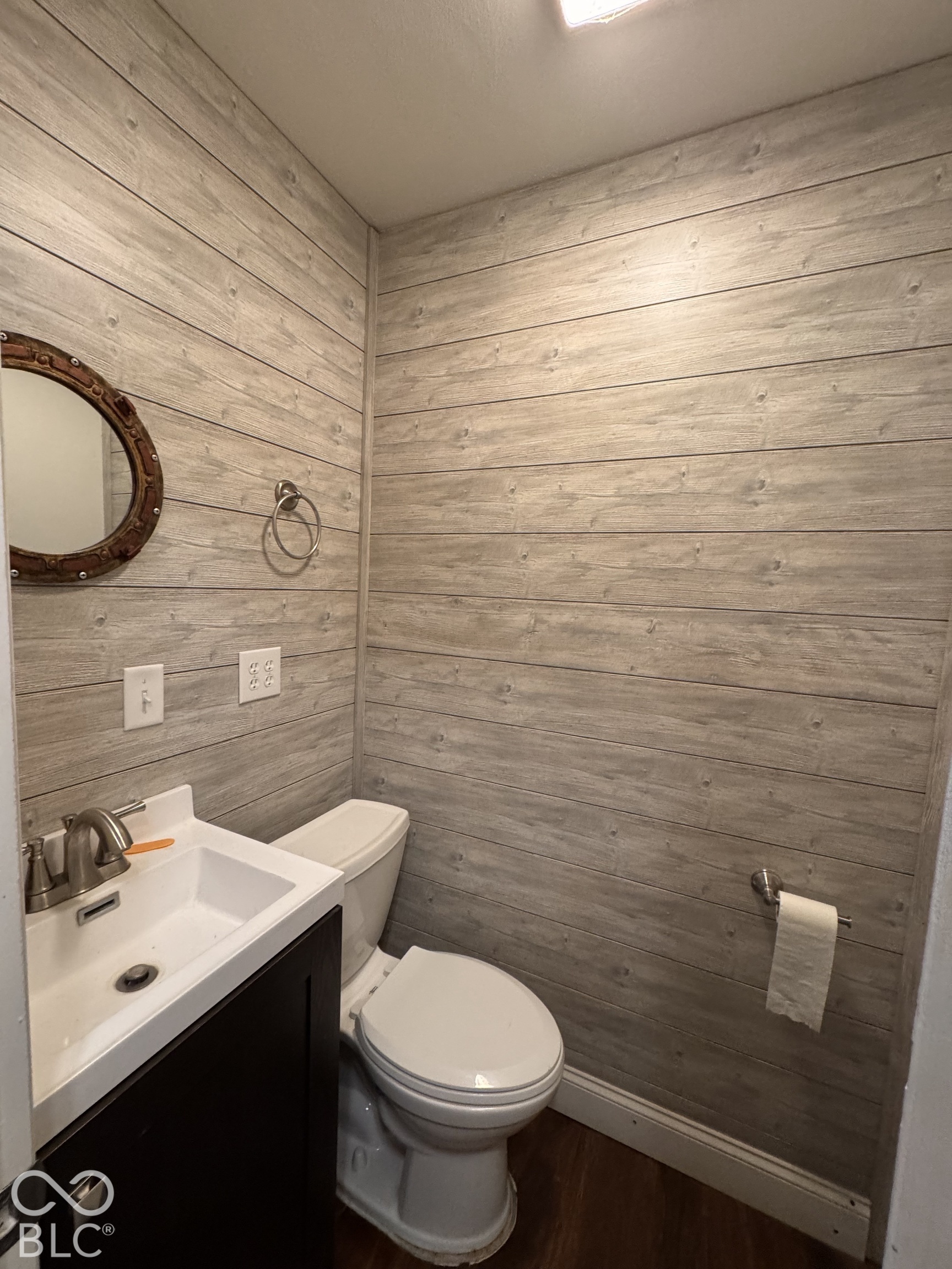Horizontal wood-finish wall paneling, dark-tone vanity cabinet, rectangular integrated basin, polished metal faucet, and circular wall-mounted mirror
