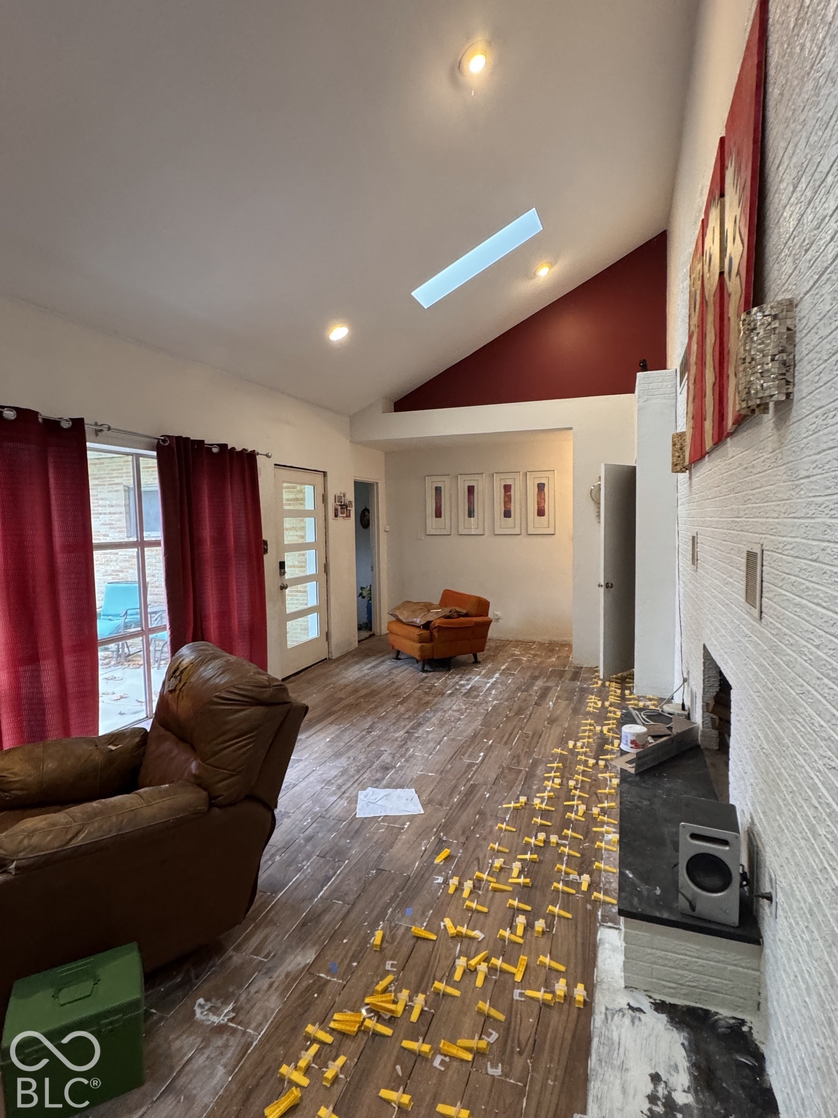 Vaulted ceilings featuring a skylight, wood-finish flooring, and a floor-to-ceiling painted brick wall with an integrated fireplace hearth