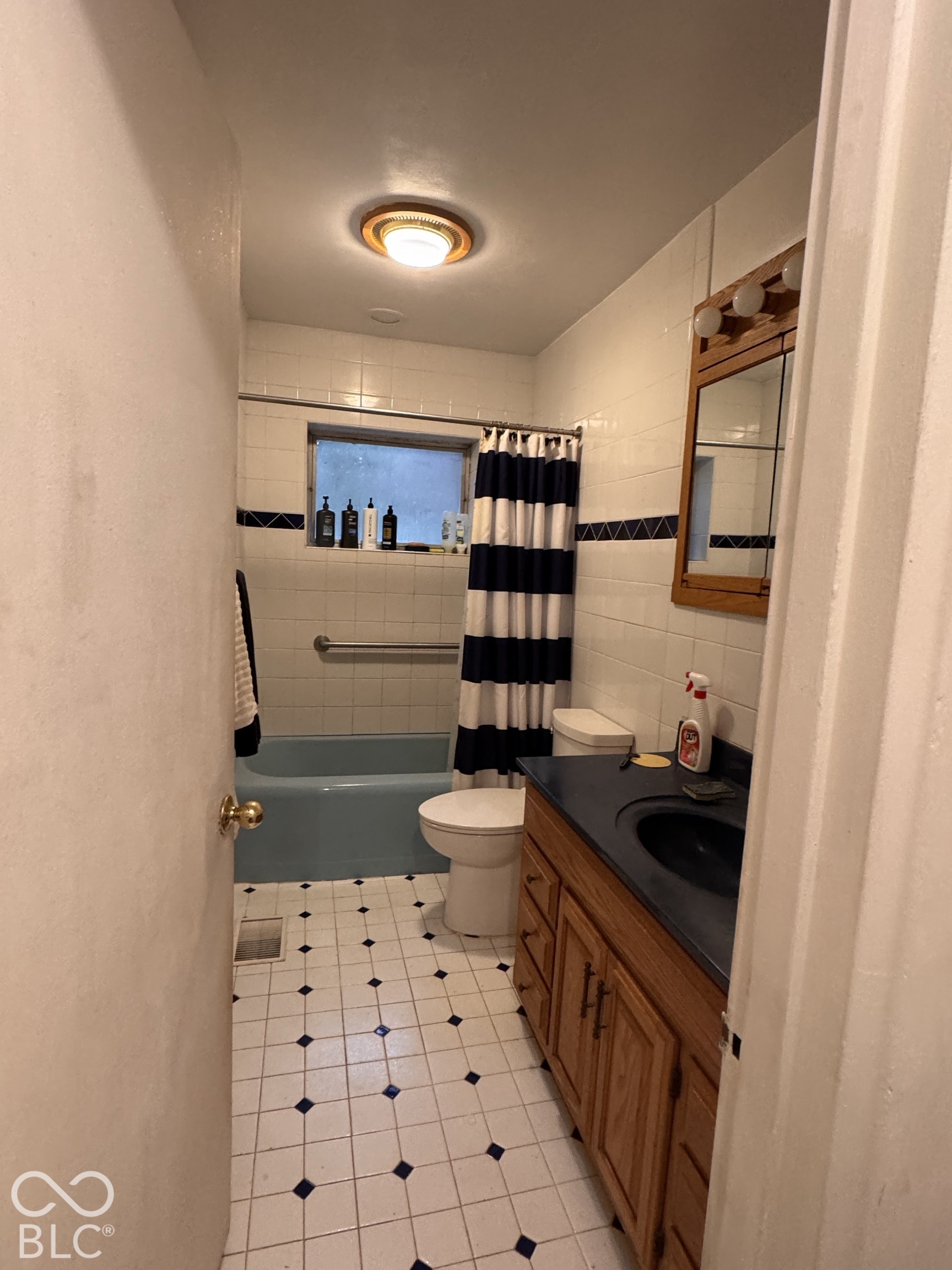 Bathroom featuring a vanity with dark countertop, built-in wooden cabinetry, wall-mounted mirror, tiled shower walls with decorative inlay, and a tub
