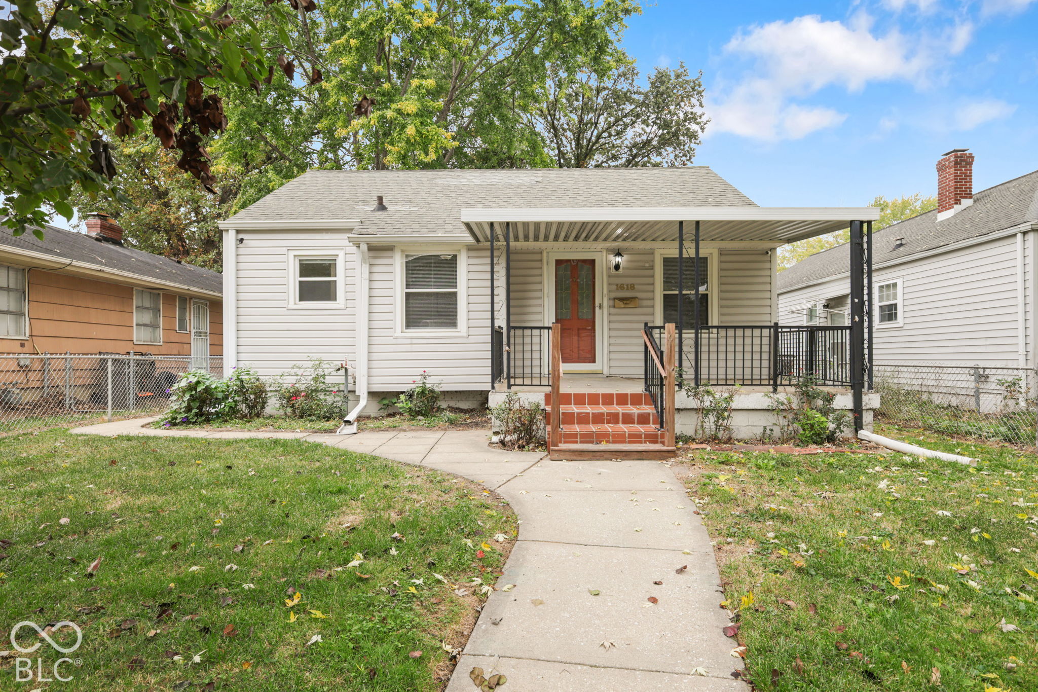 Exterior featuring light-toned horizontal siding, a covered front porch with metal railing, brick steps, and a concrete walkway