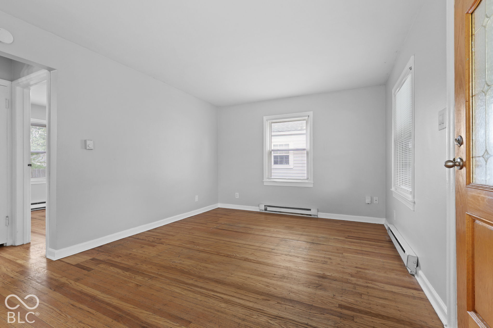 Interior space featuring wood-finish flooring, light-toned wall paint, multiple windows, and a glass-paneled wooden exterior door