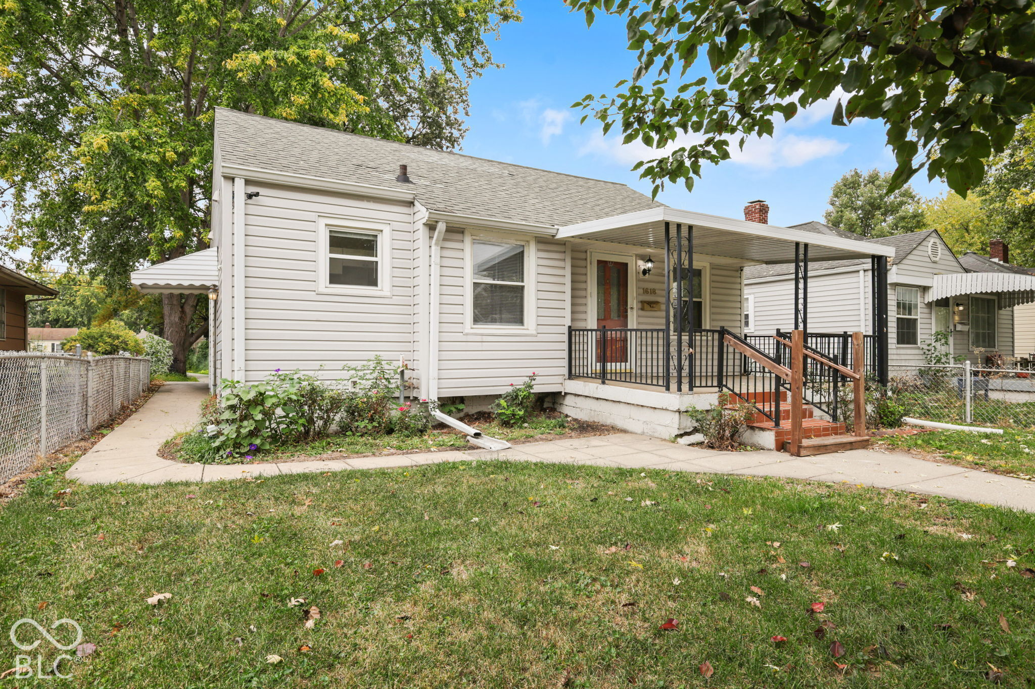 Exterior featuring horizontal siding, a covered front porch with metal railing, concrete walkway, and an attached side awning