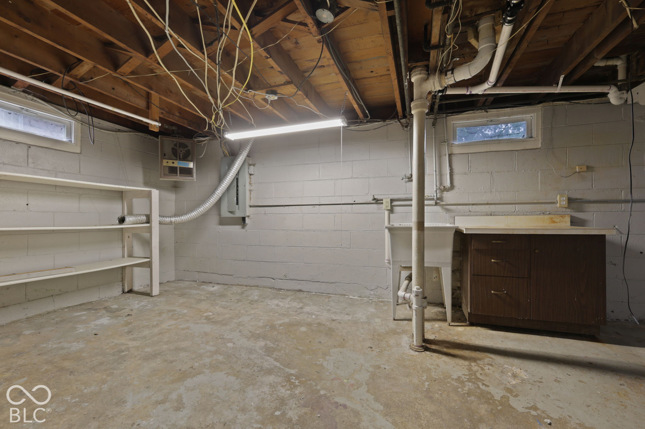 Unfinished space featuring painted concrete block walls, concrete flooring, built-in wooden shelving, a utility sink, and wood-finish storage cabinetry