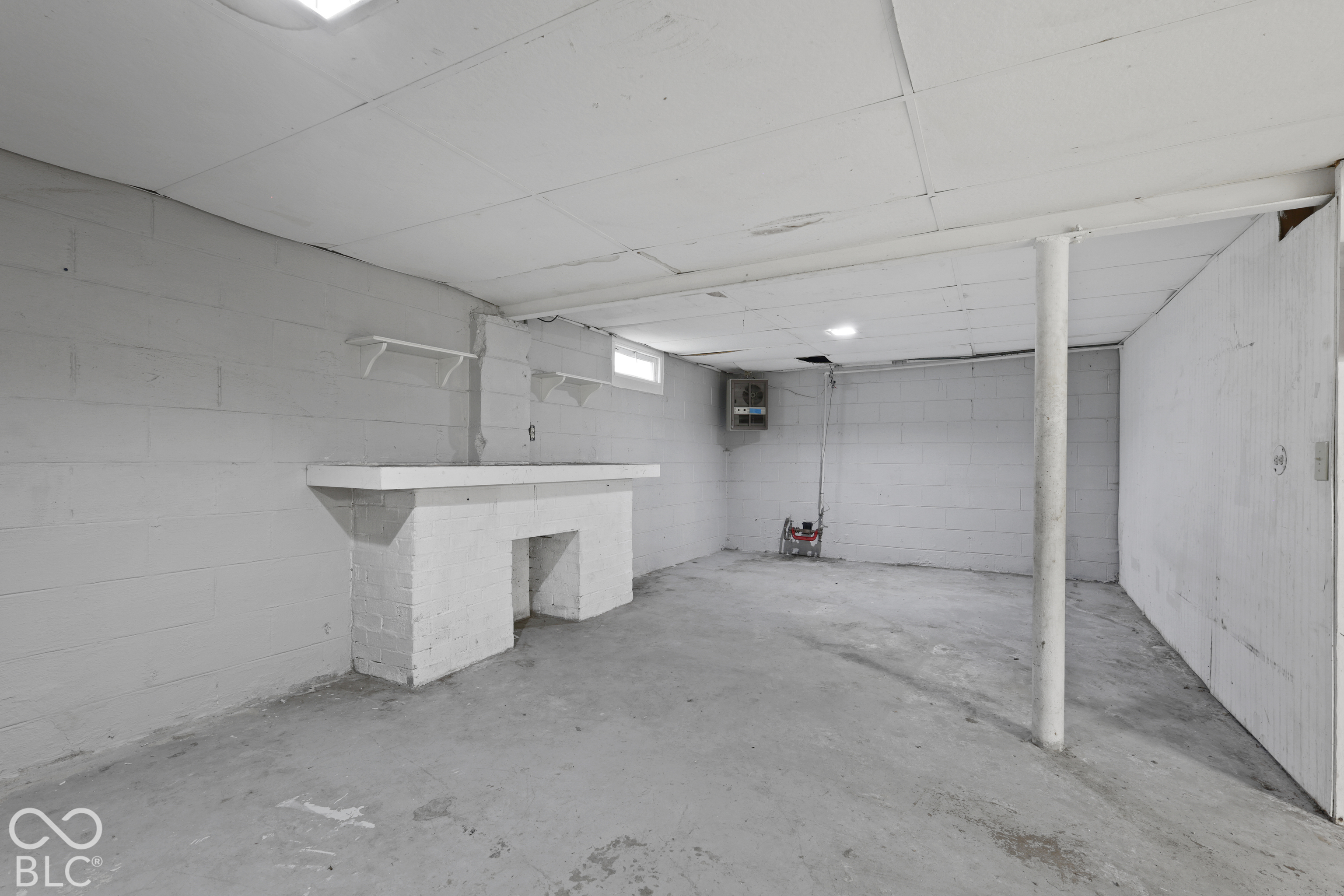 Painted concrete block walls, ceiling tile system, concrete flooring, built-in masonry mantel, and vertical structural support column