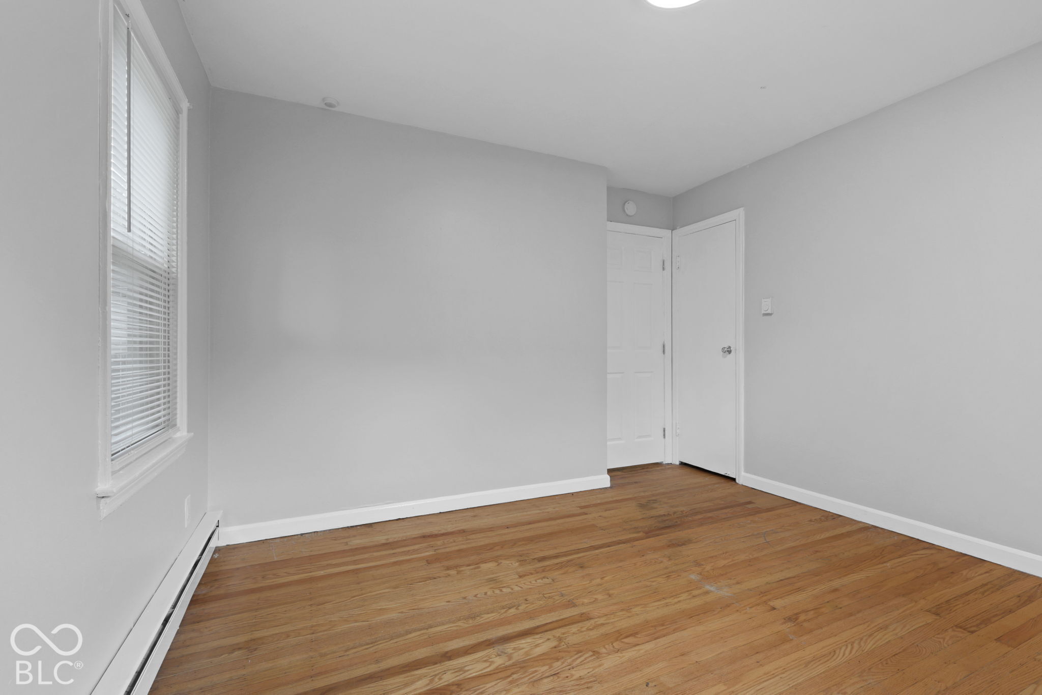 Room featuring wood-finish flooring, neutral walls, a single-hung window with blinds, and two solid-core paneled doors