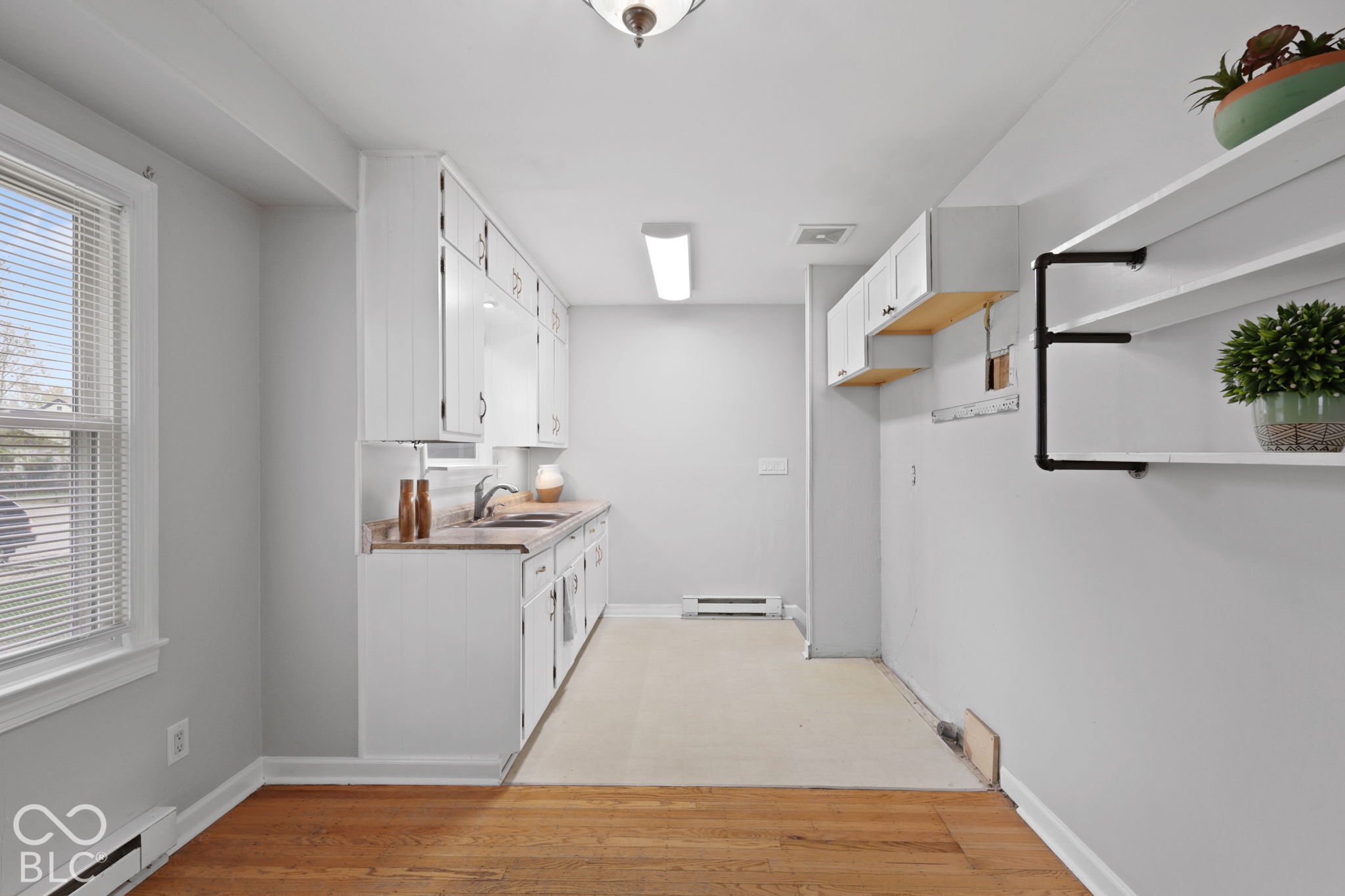 Kitchen featuring white cabinetry, wood-finish flooring, a stainless steel sink with a faucet, and industrial-style wall-mounted shelving