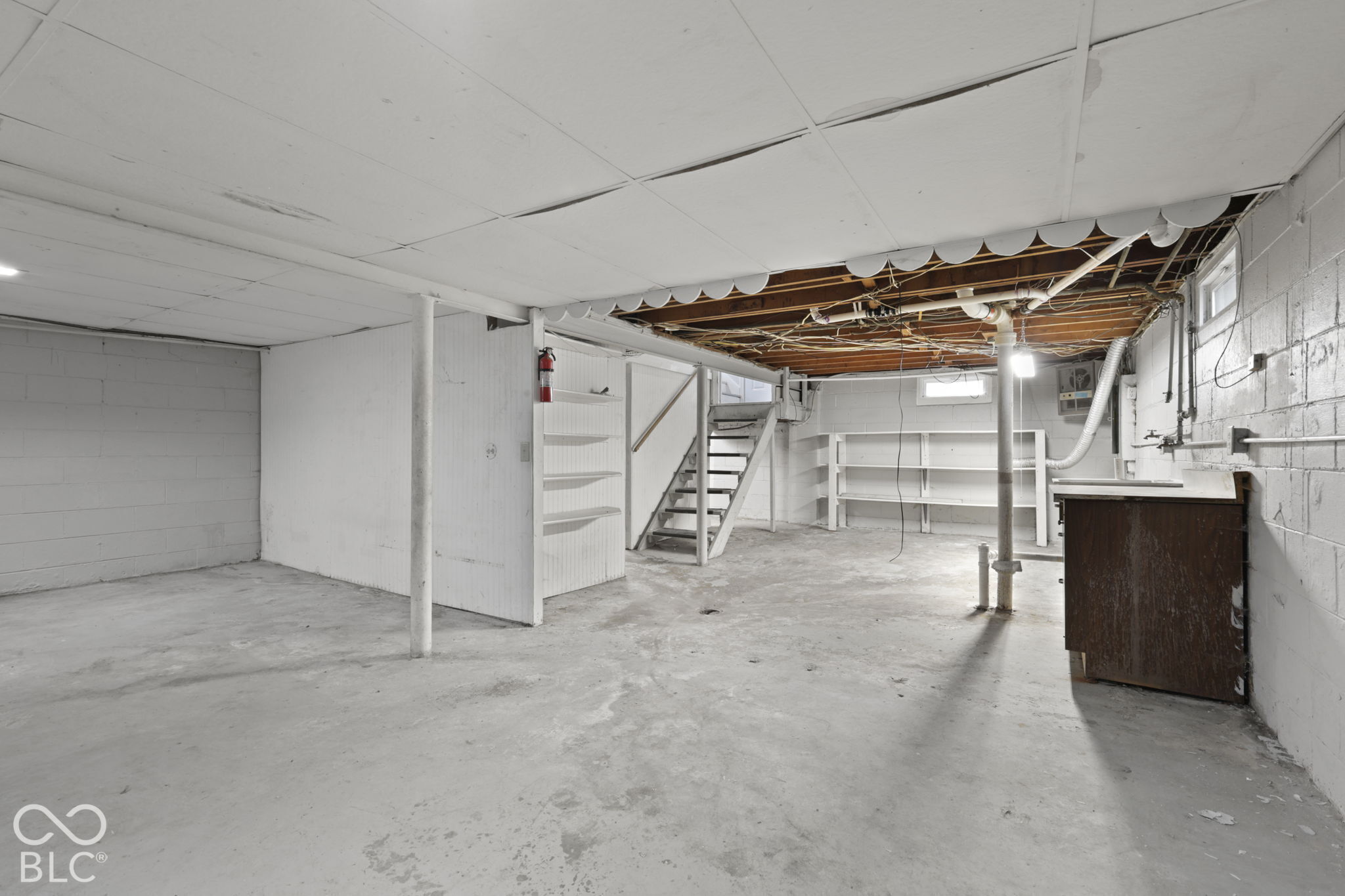 Unfinished lower level featuring concrete flooring, painted masonry walls, built-in wooden shelving, and open joist ceiling construction