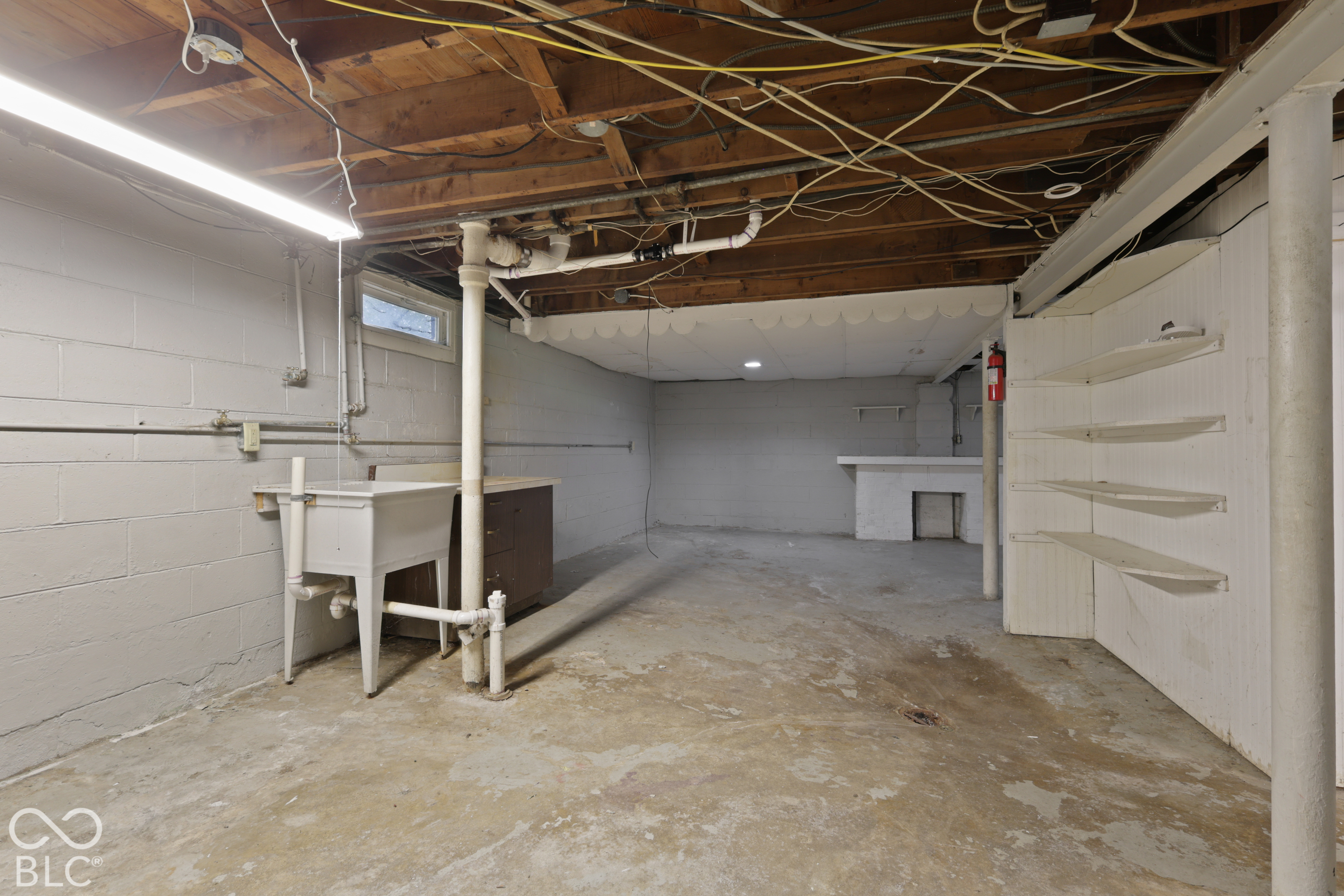 Lower level space featuring painted masonry walls, built-in open shelving, a utility sink, and exposed ceiling joists