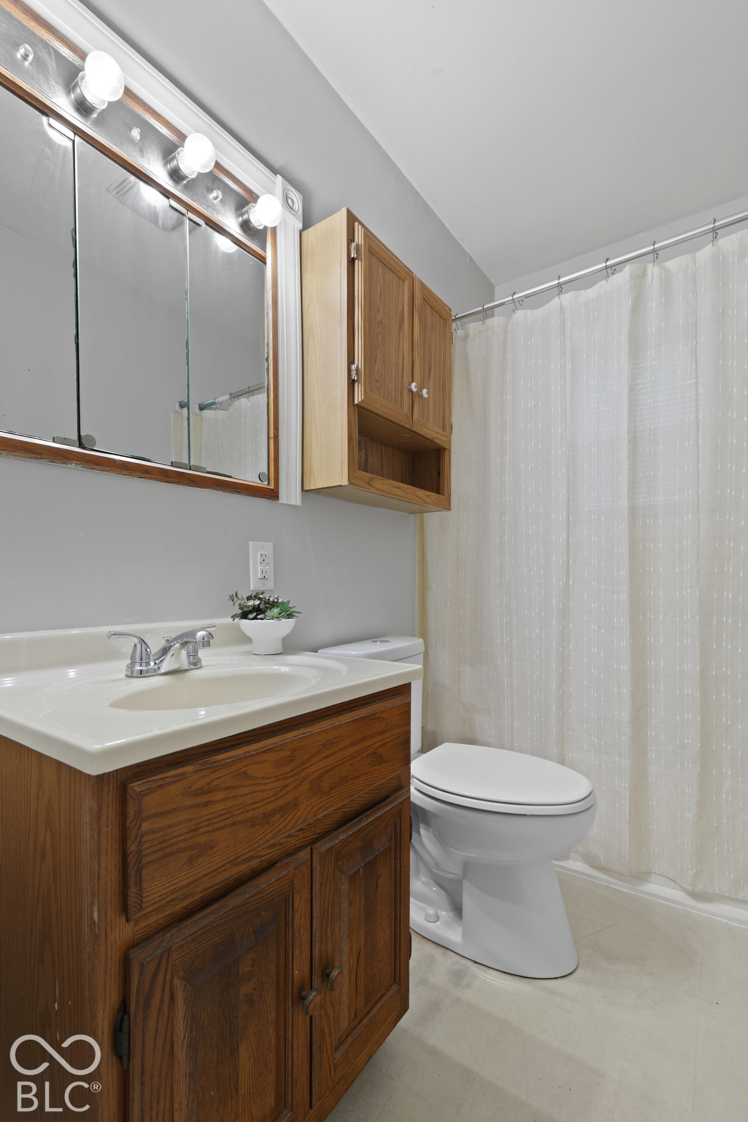 Bathroom featuring a wood-finish vanity with a molded countertop, three-light wall-mounted fixture, wall-mounted wooden cabinetry, and a chrome dual-handle faucet