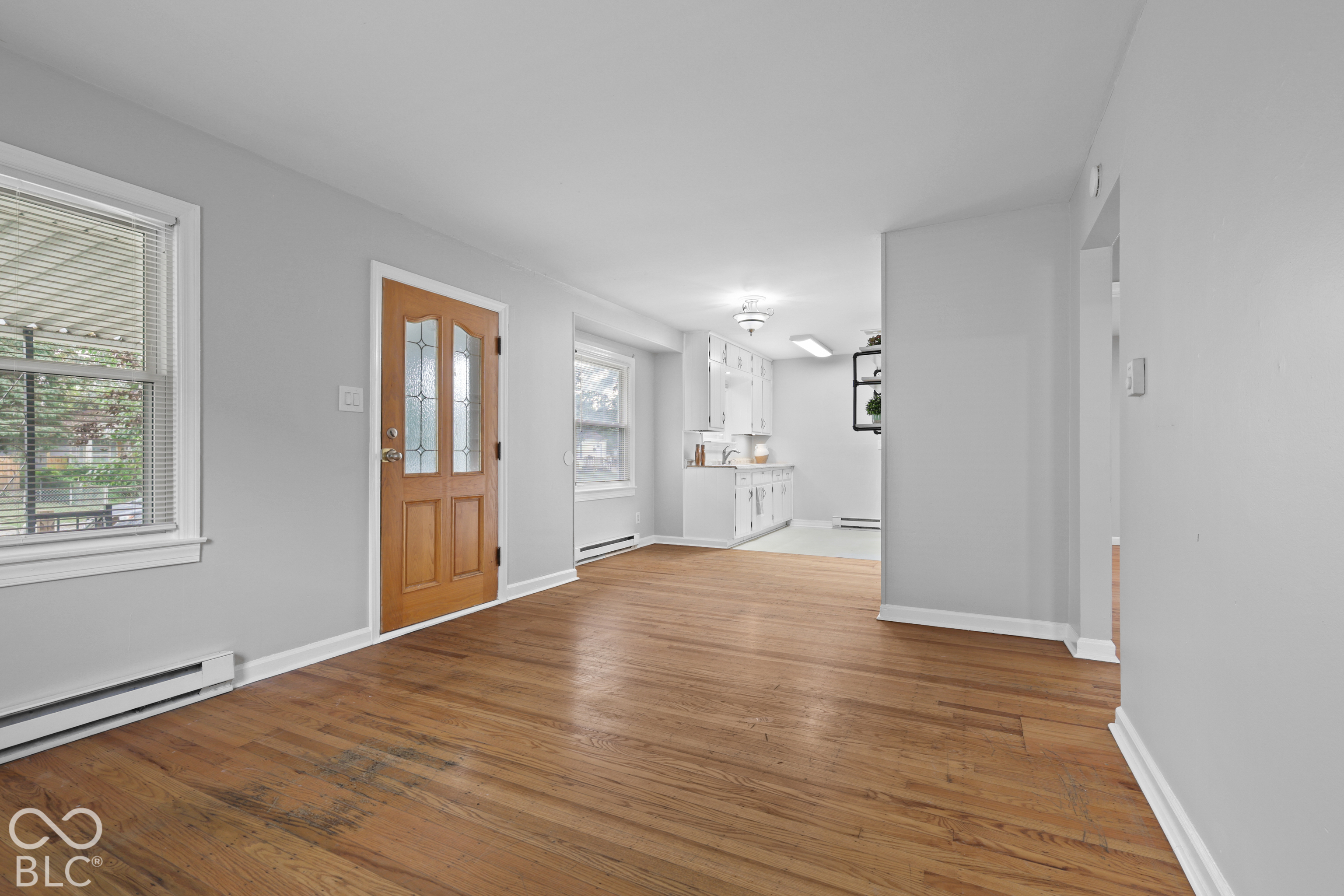Interior space featuring hardwood flooring, a natural wood-finish door with decorative glass inlay, and white cabinetry in the kitchen area