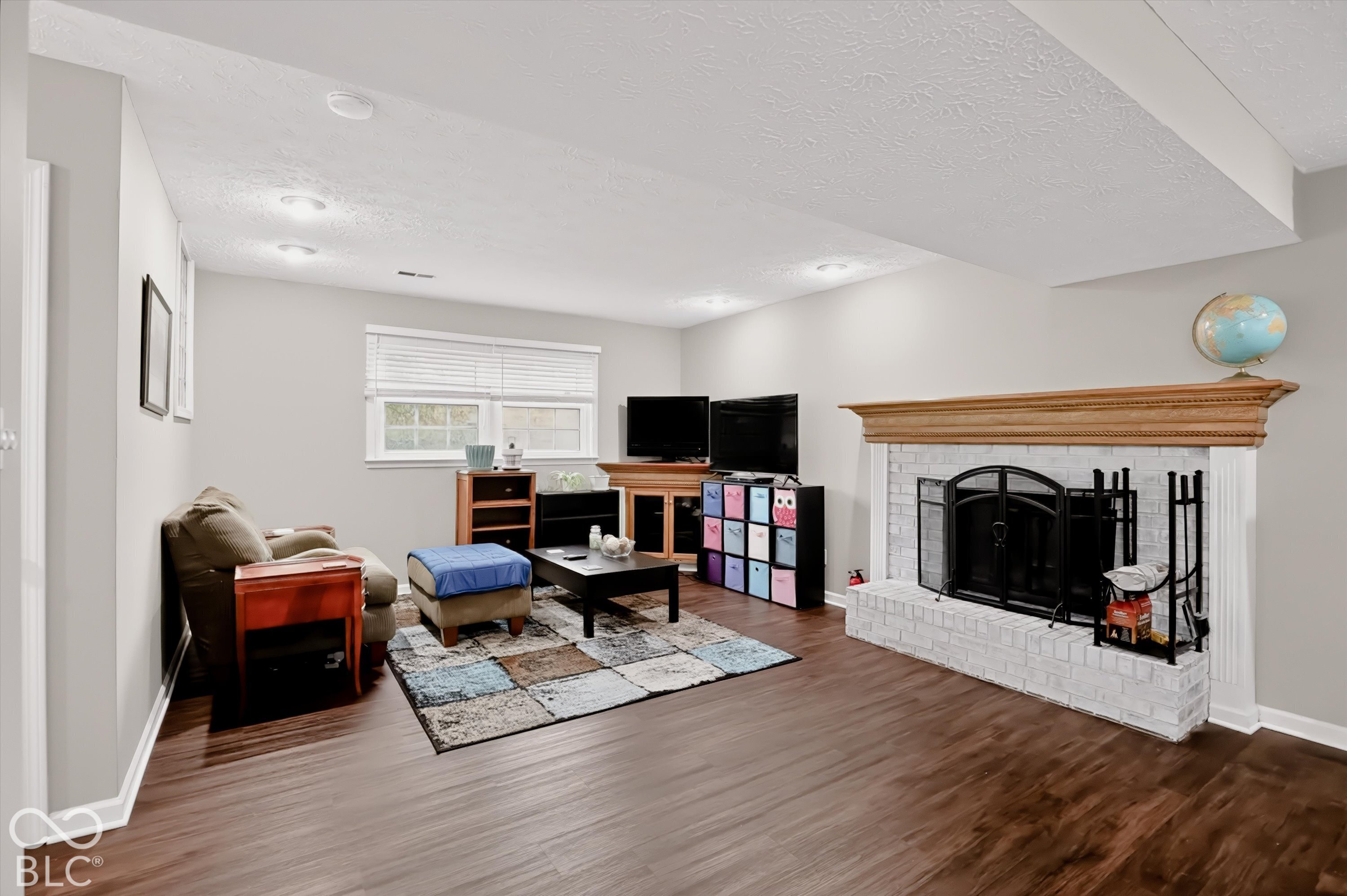 Painted brick fireplace with a wood mantel, recessed lighting, and wood-finish flooring