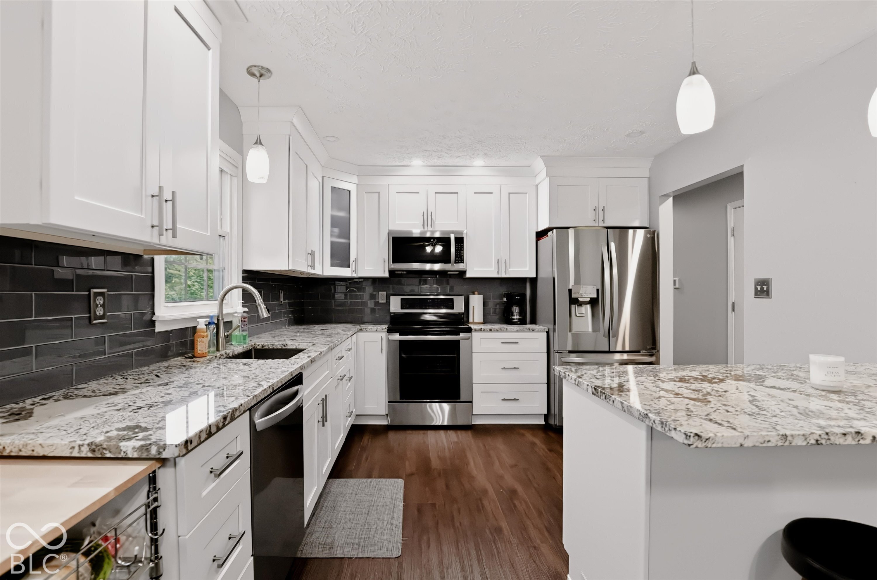 Kitchen featuring white shaker cabinetry, stone countertops, dark subway tile backsplash, stainless steel appliances, and wood-finish flooring