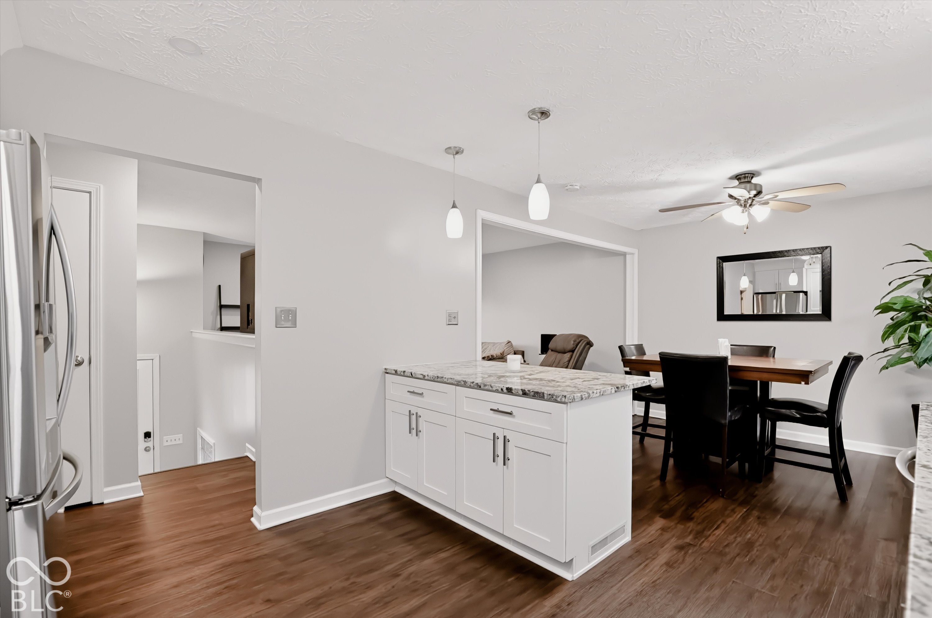 Kitchen island featuring white shaker-style cabinetry, stone-finish countertop, dual pendant lighting, and wood-finish flooring