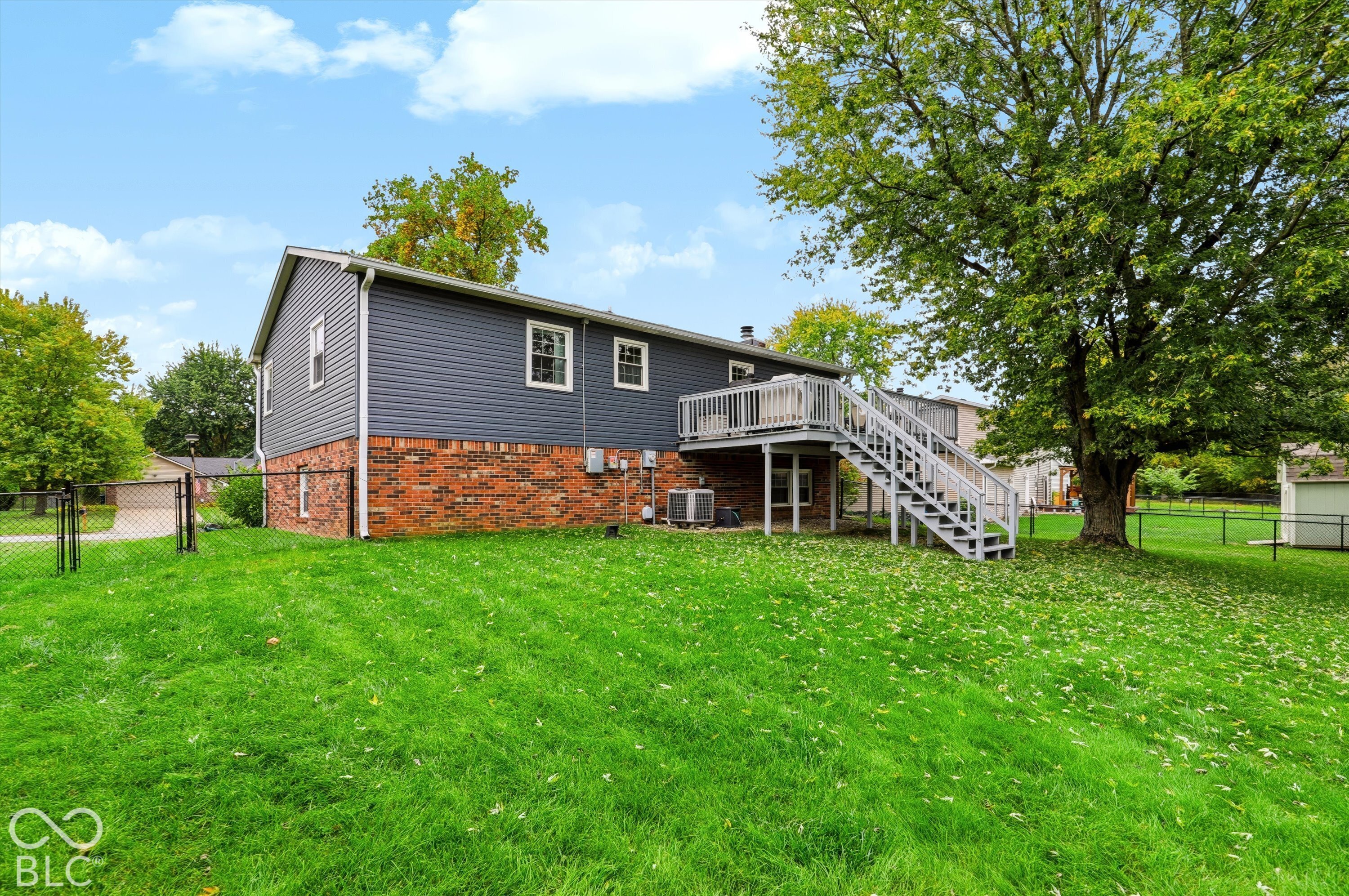 Exterior featuring charcoal-colored siding, a brick foundation, a wood-constructed deck, and a fenced-in backyard with mature trees