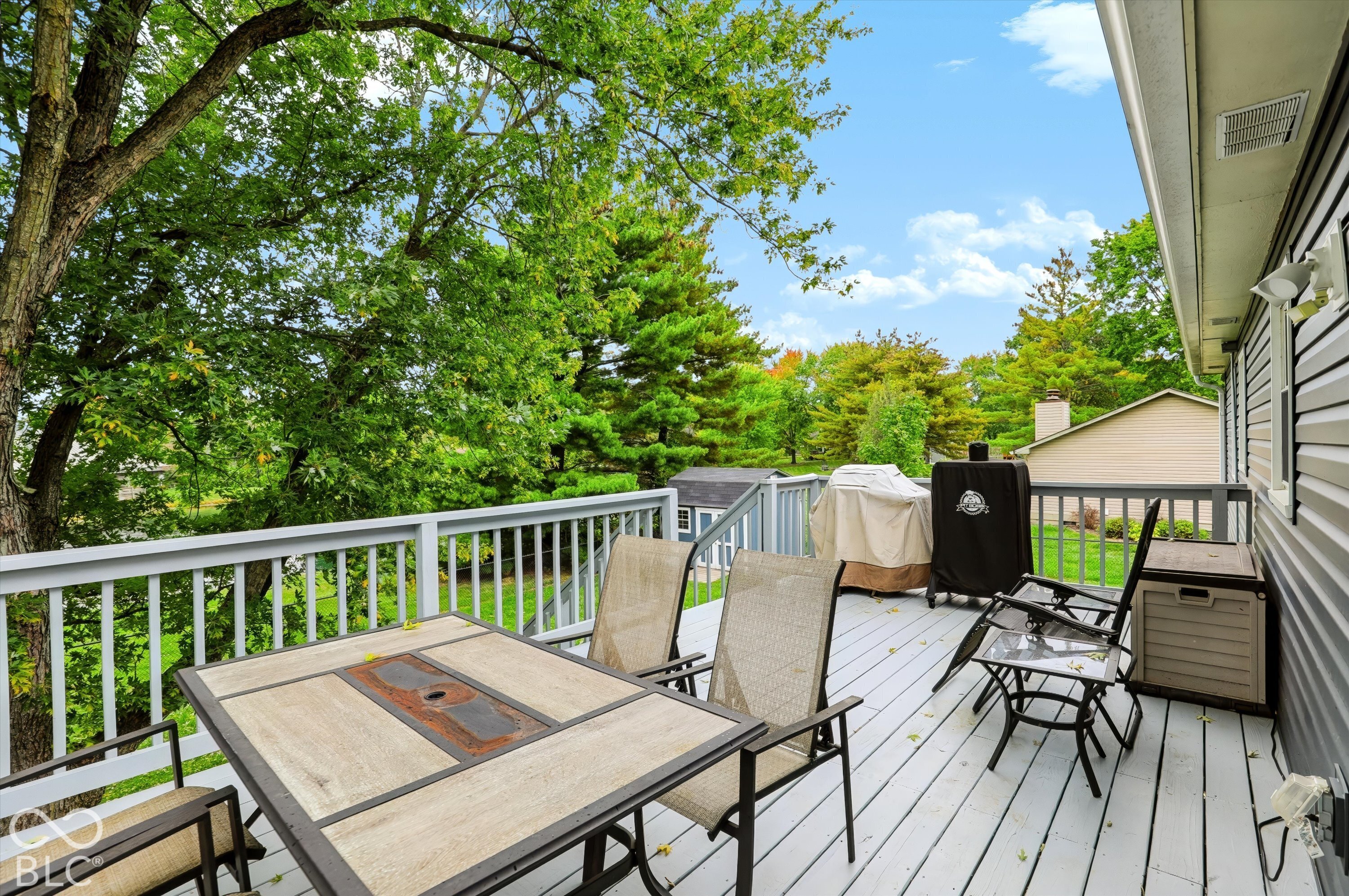Elevated deck featuring light-colored wood decking, white baluster railings, and mature surrounding trees