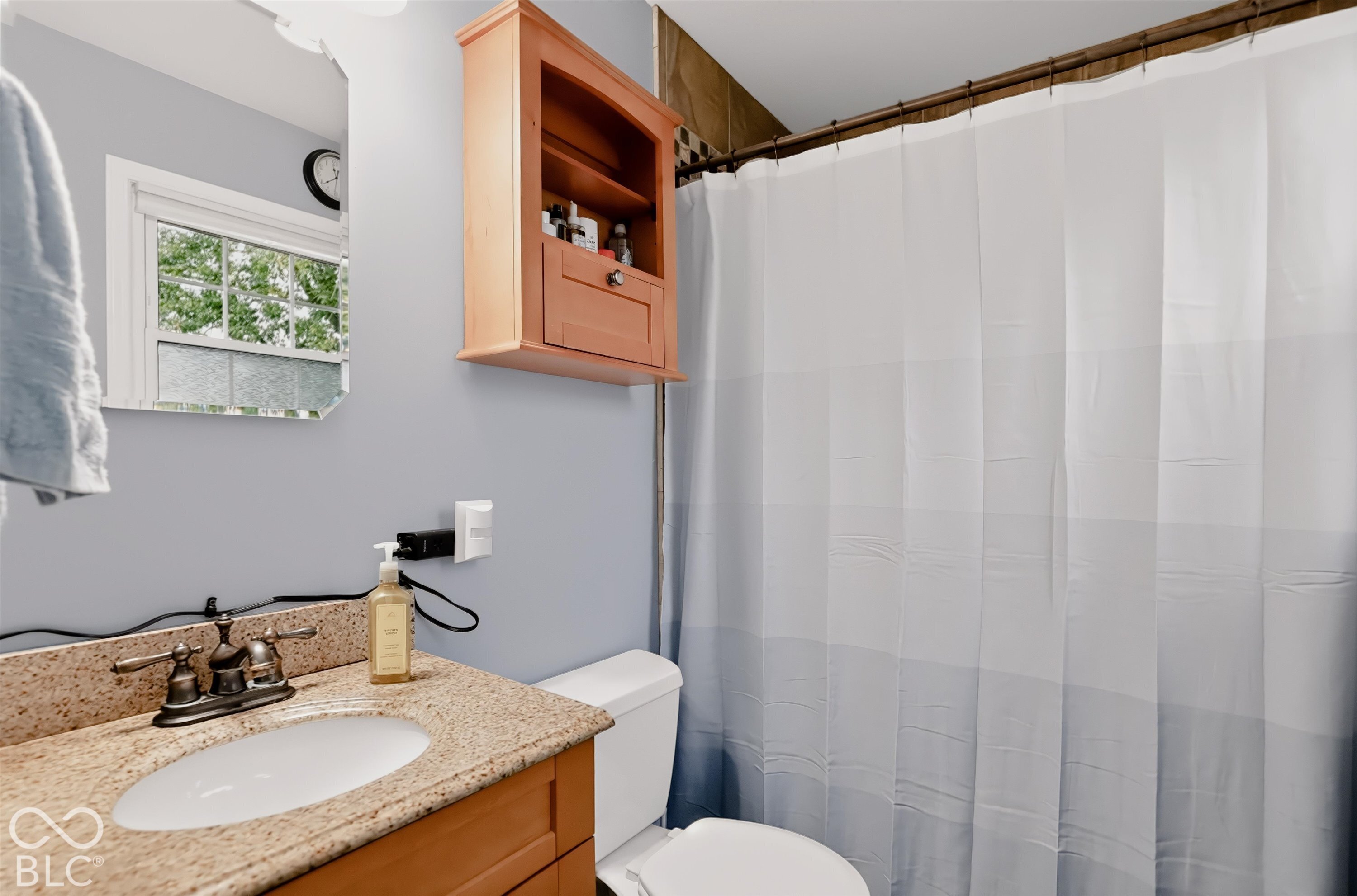 Bathroom featuring a stone-composite countertop with an integrated basin, wooden cabinetry, wall-mounted storage unit, and polished metal faucet fixtures