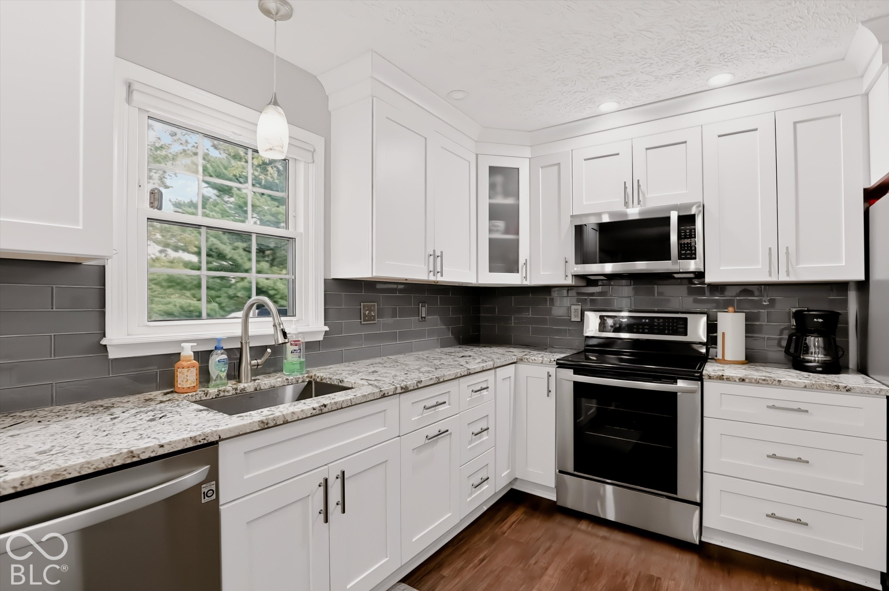 Kitchen featuring white shaker-style cabinetry, stone-finish countertops, grey subway tile backsplash, stainless steel appliances, and wood-finish flooring