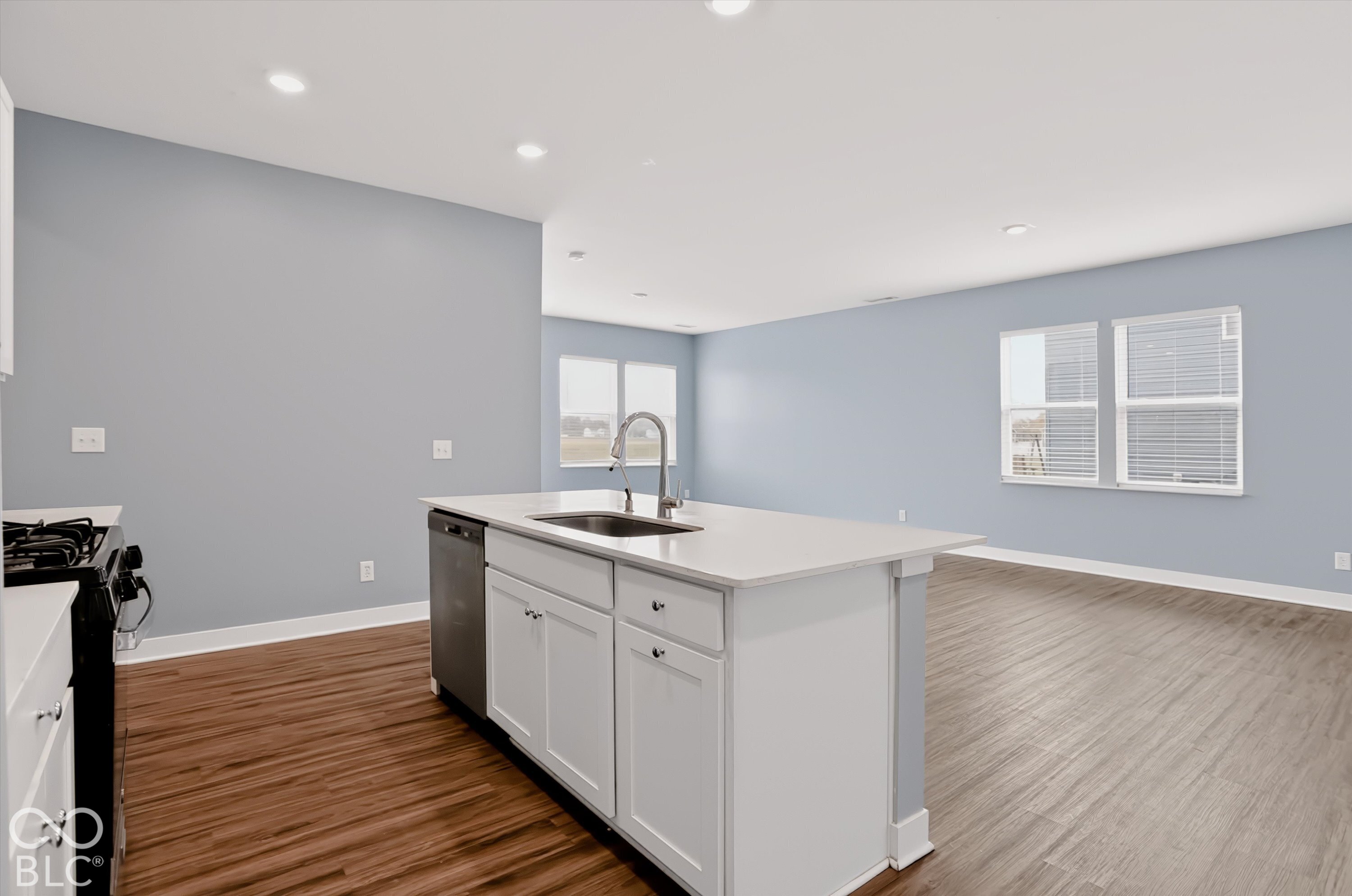 Kitchen featuring a central island with an integrated sink, stone-surface countertop, white cabinetry, recessed lighting, and wood-finish flooring