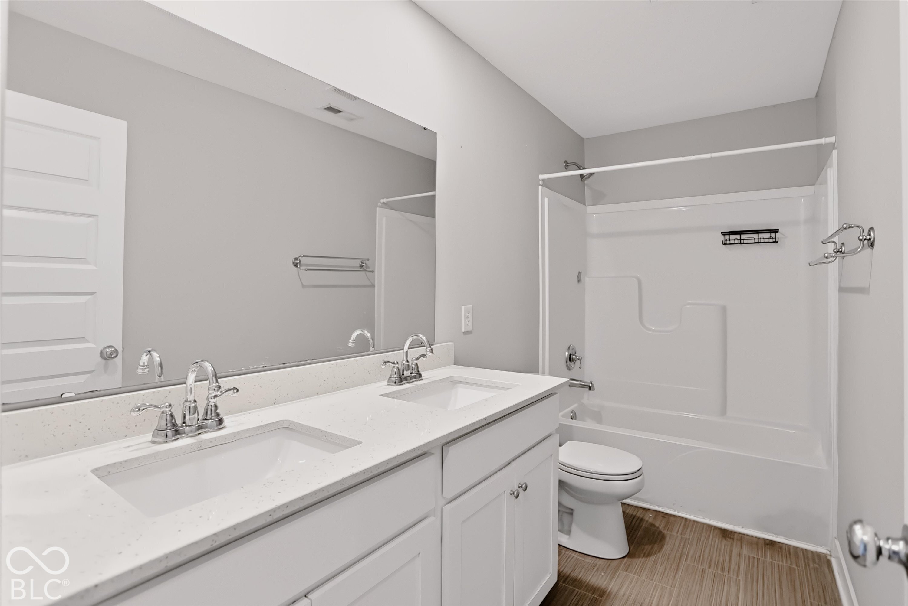 Dual-sink vanity with a solid-surface countertop, white shaker-style cabinetry, large wall-mounted mirror, and tub-shower combination with tile-patterned surround