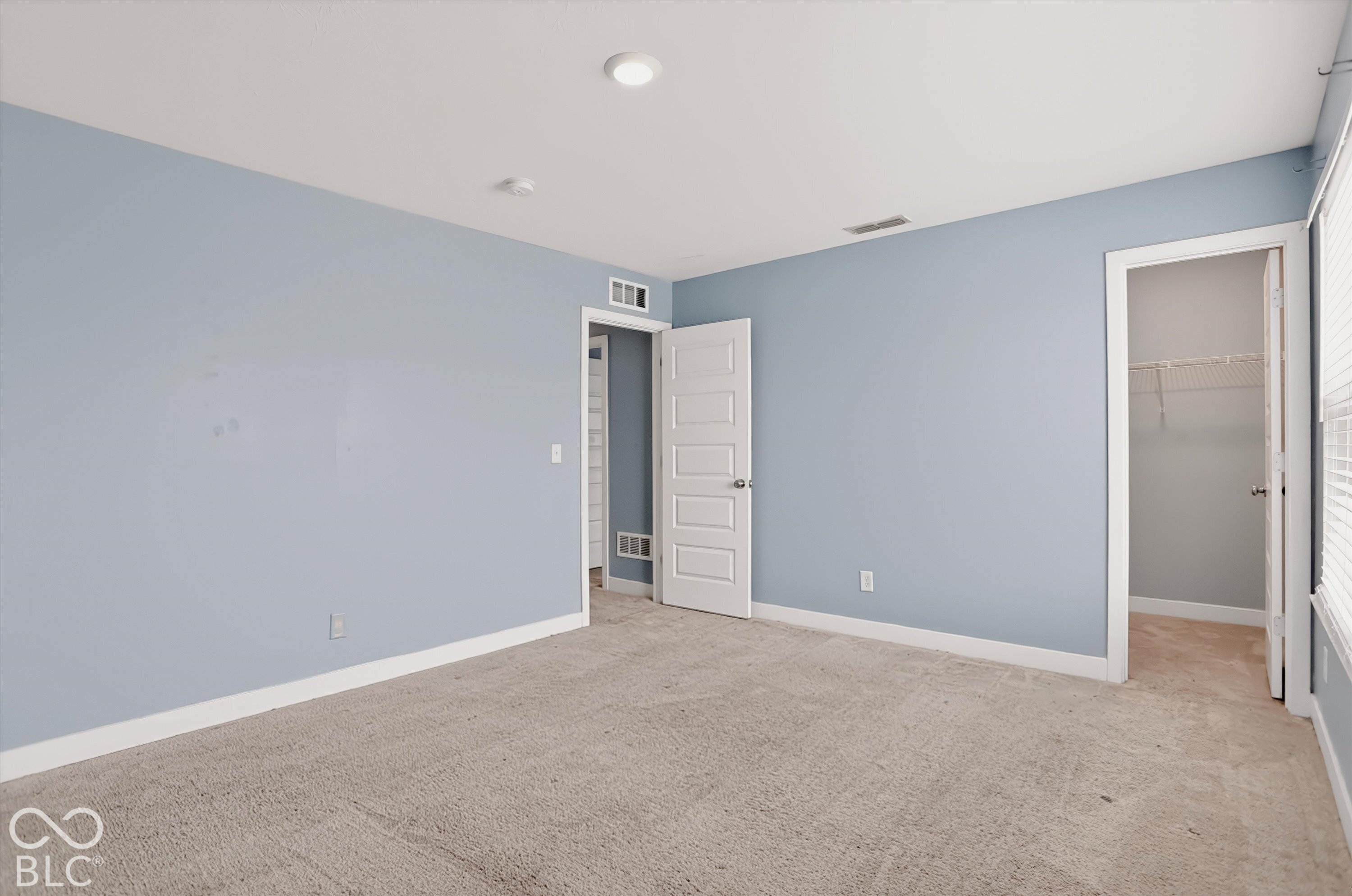 Neutral-toned wall paint, recessed lighting, carpeted flooring, five-panel interior door, and walk-in closet with built-in wire shelving