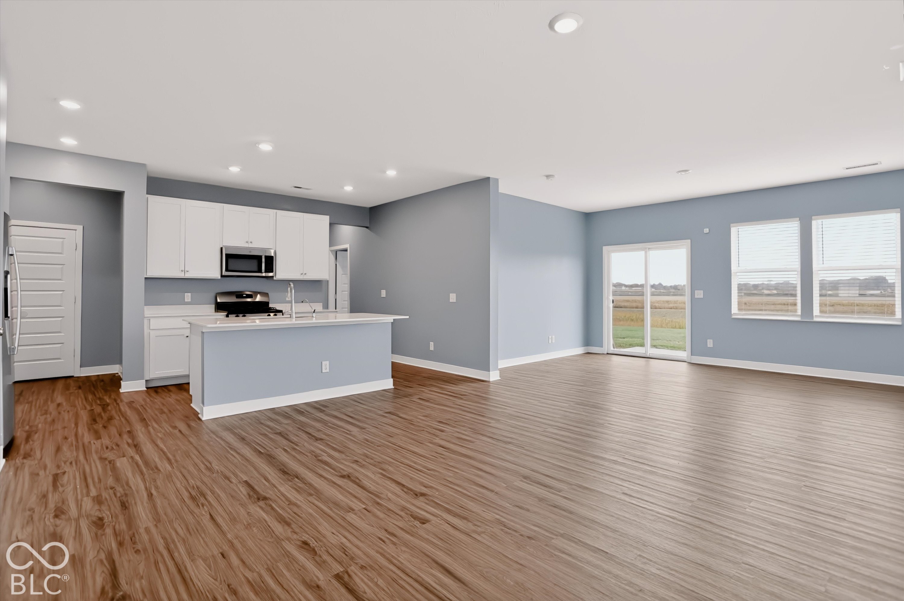 Open-concept area featuring wood-finish flooring, white cabinetry, a kitchen island with a built-in sink, recessed lighting, and sliding glass doors