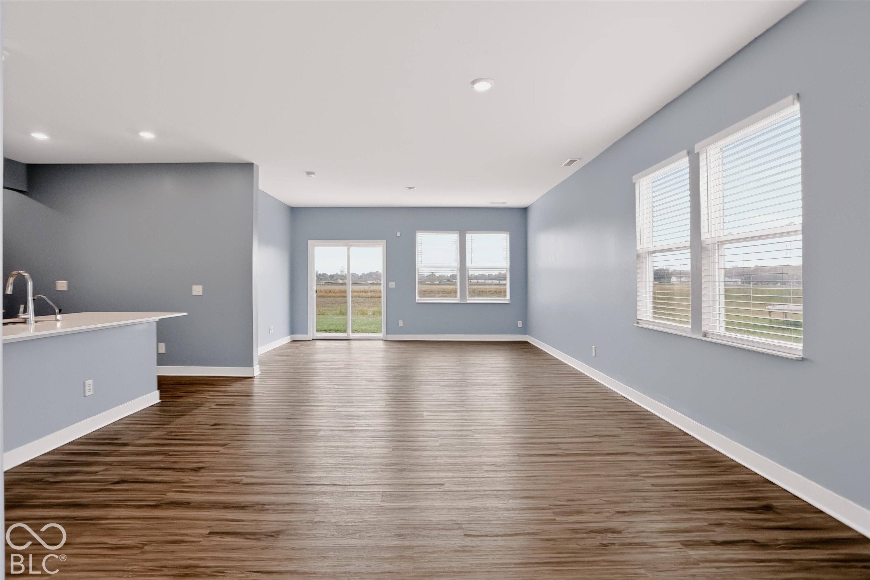 Open-concept interior featuring wood-finish flooring, recessed lighting, expansive windows with blinds, and sliding glass doors
