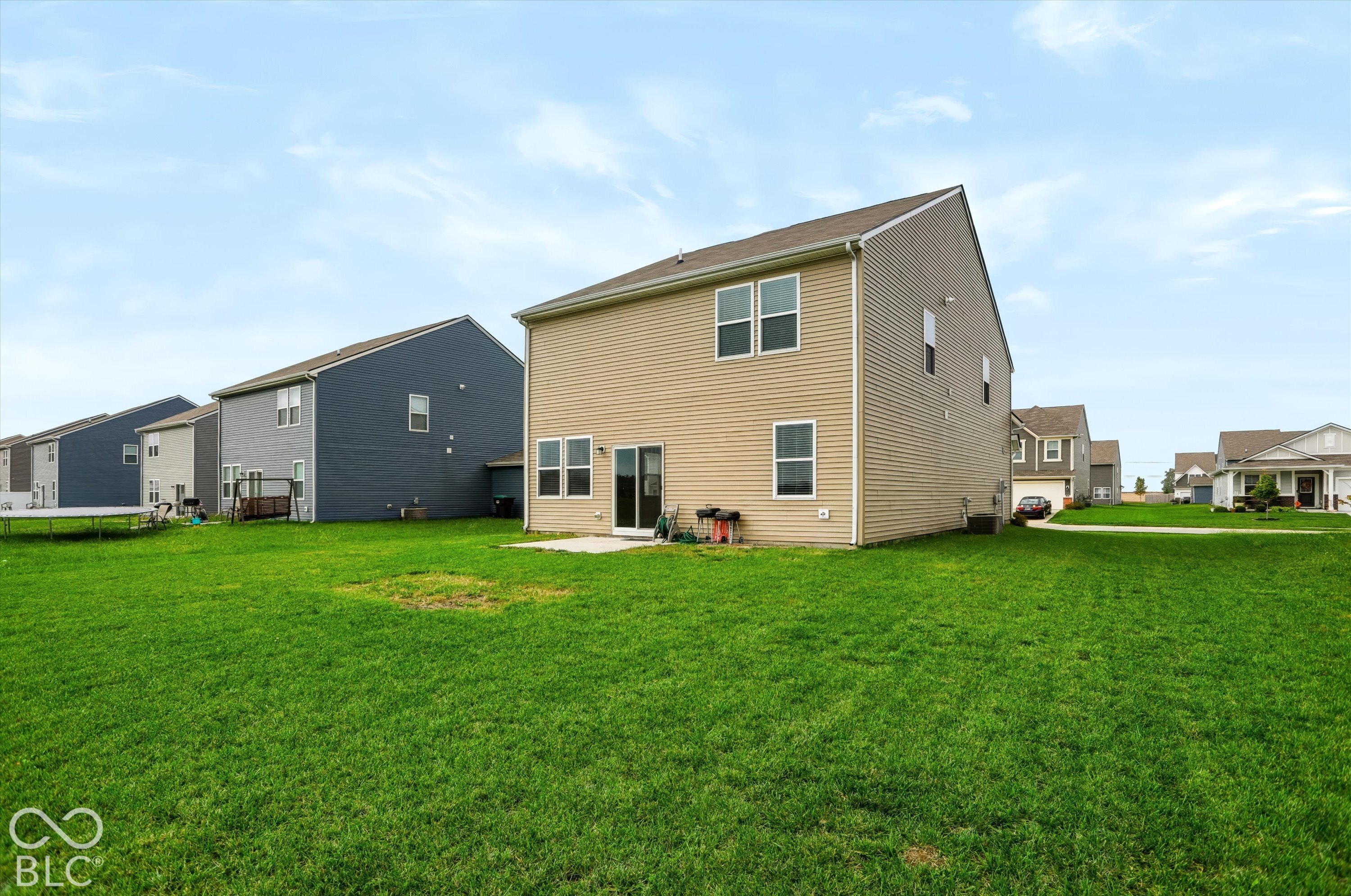 Rear exterior featuring tan vinyl siding, a concrete patio, and an expansive lawn