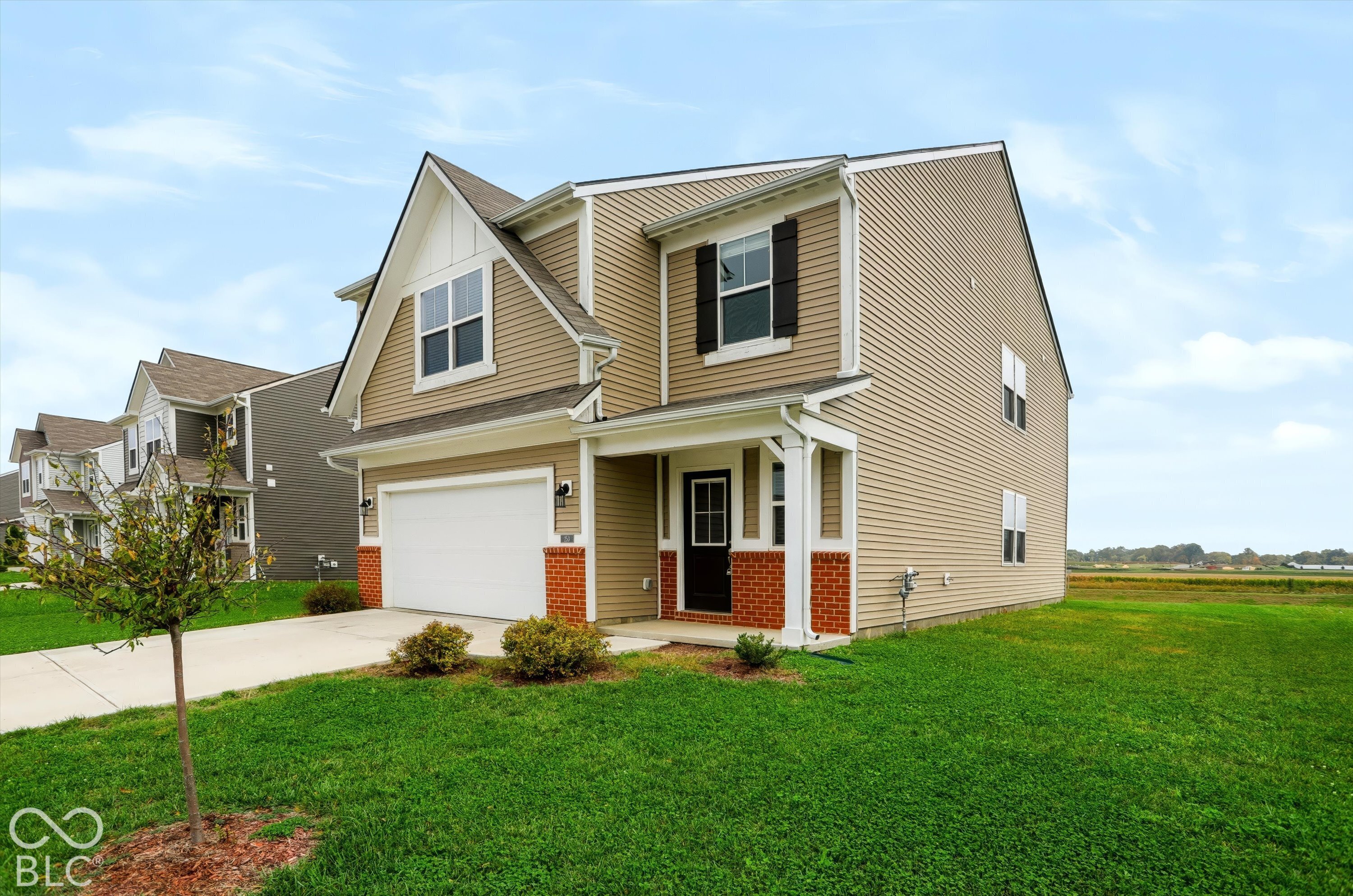 Two-story residence featuring tan vinyl siding, decorative red brick facade accents, a front-facing gable, a covered entryway, and a concrete driveway