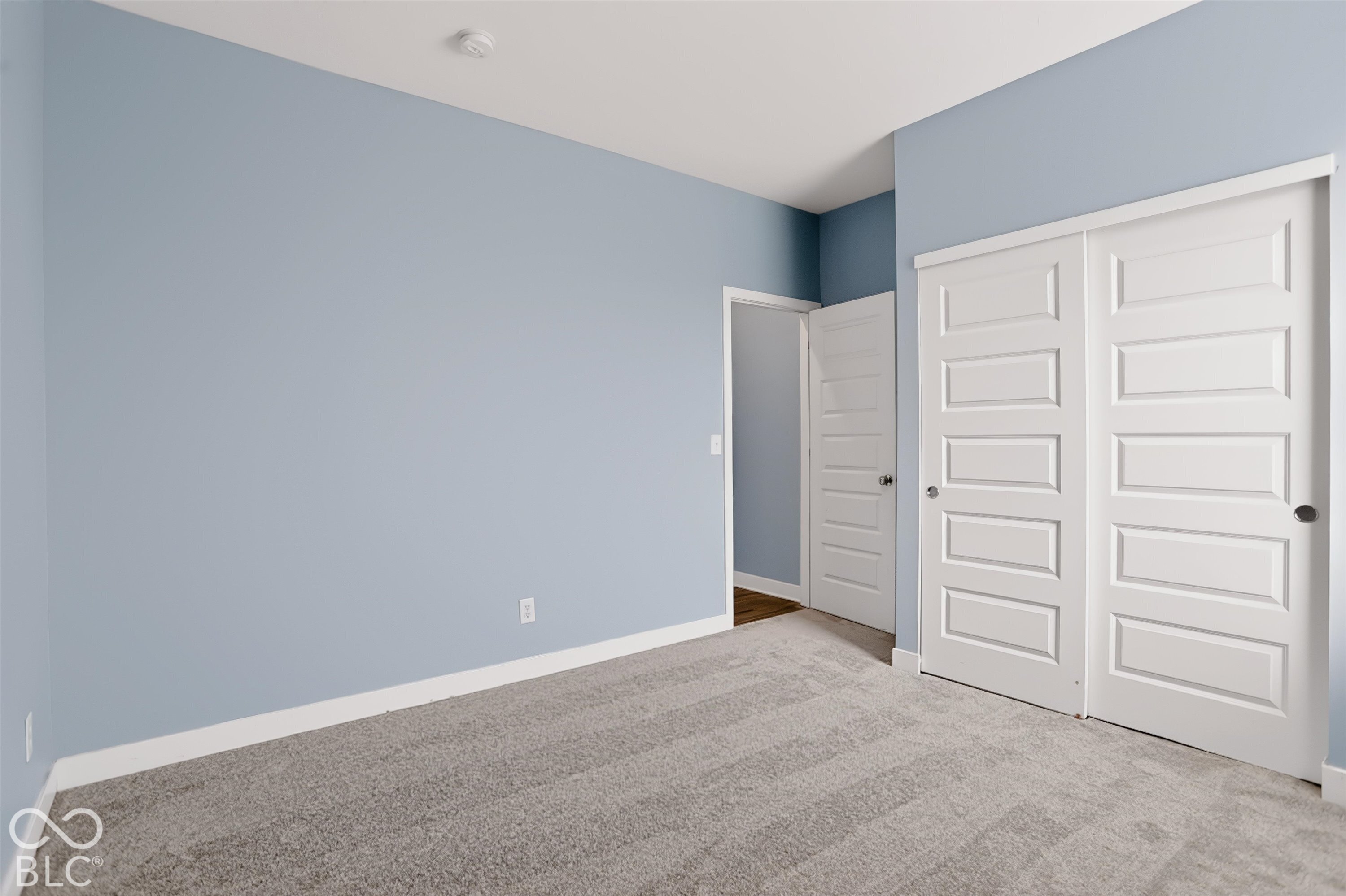 Room featuring neutral carpeting, light blue wall paint, and a sliding-door closet with five-panel door detailing