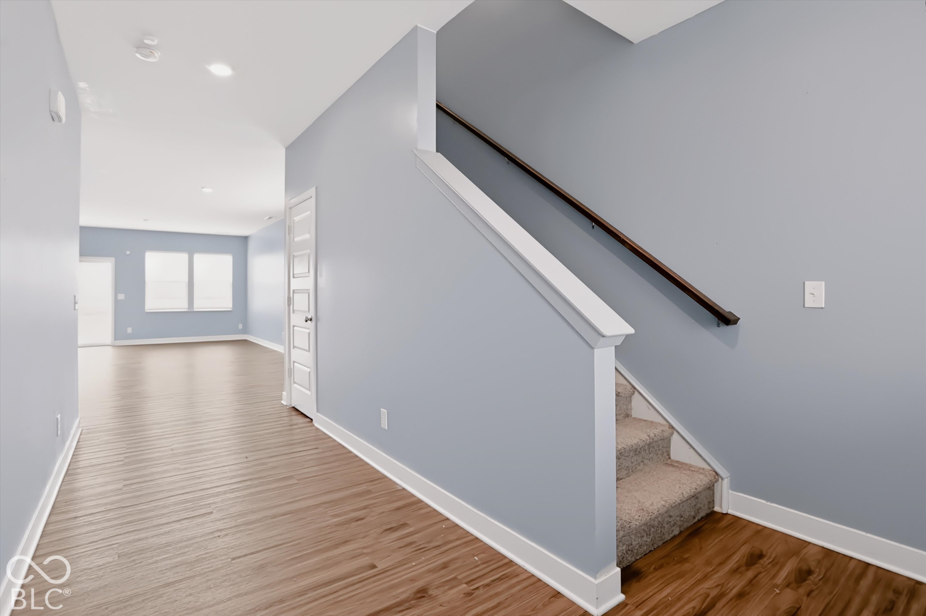 Interior space featuring wood-finish flooring, staircase with a dark wood handrail, recessed lighting, and multi-panel interior door