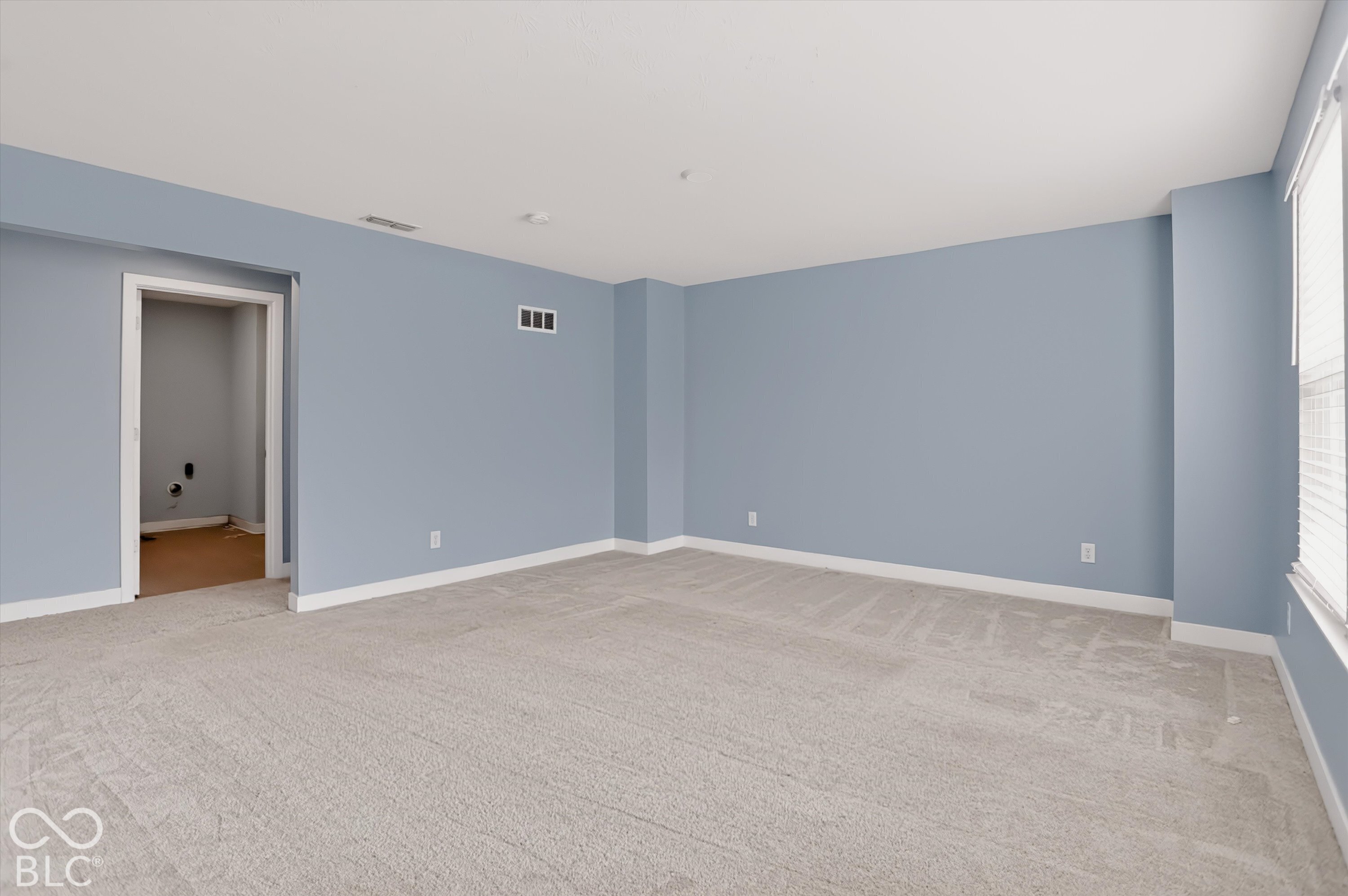 Spacious room featuring neutral carpeting, light-toned wall paint, and windows with integrated blinds