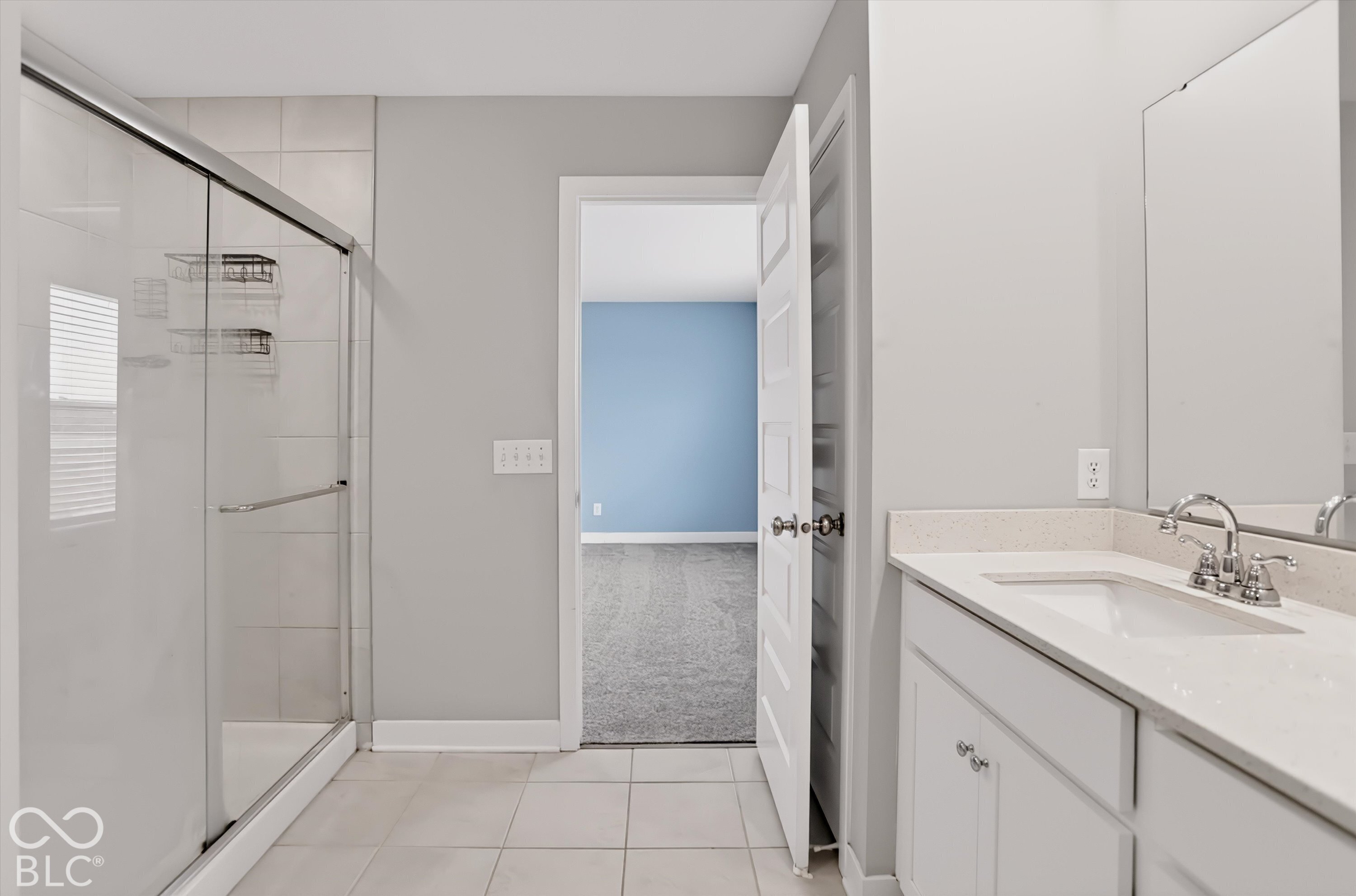 Bathroom featuring a shower stall with a glass enclosure, white vanity with stone-composite countertop, undermount sink, and tile flooring