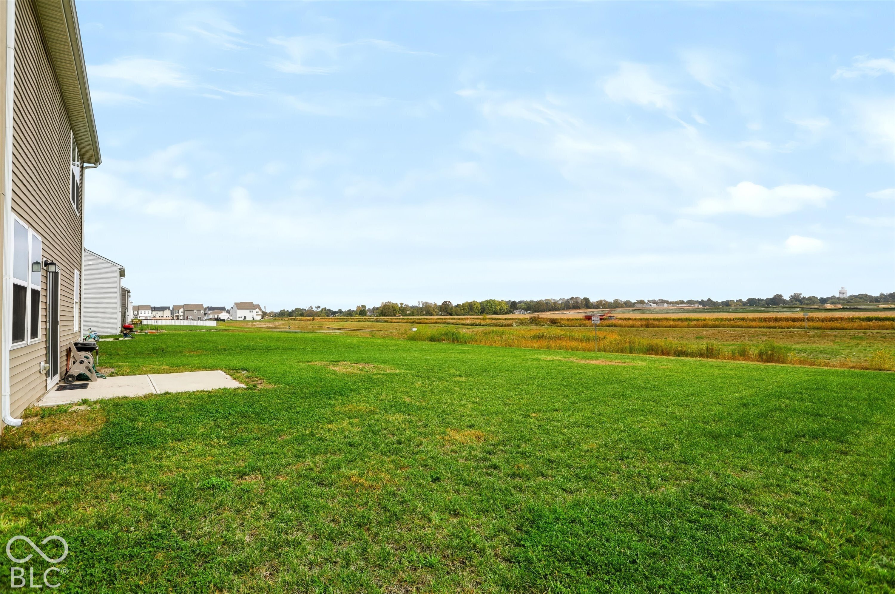 Rear exterior featuring horizontal vinyl siding, a concrete patio, and an expansive lawn bordering open acreage