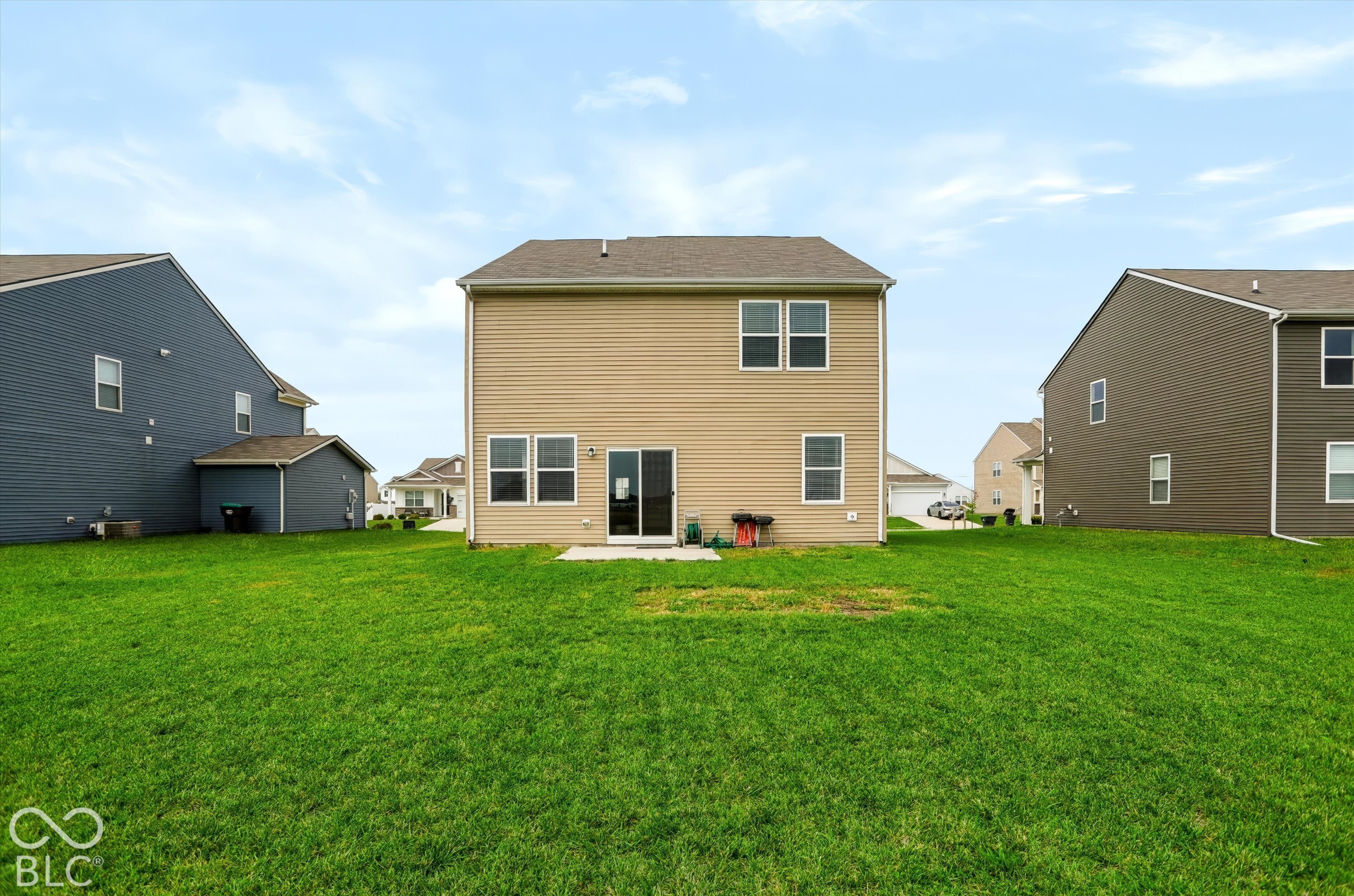 Two-story exterior with vinyl siding, shingle roof, concrete patio, and rear sliding glass door, set on a grass lawn