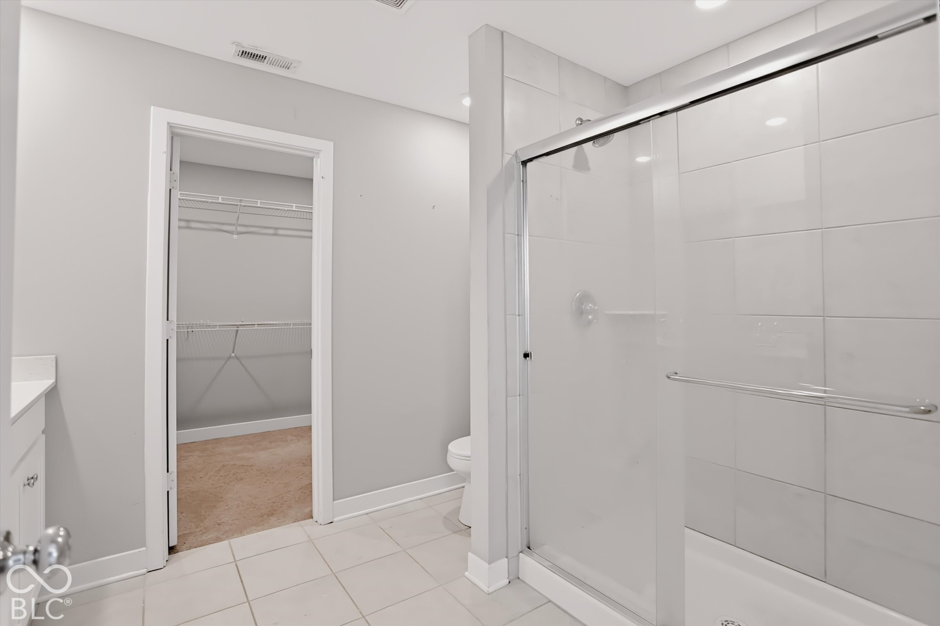 Shower with large-format wall tile and glass sliding door, porcelain tile flooring, built-in vanity with solid surface countertop, and walk-in closet with built-in shelving