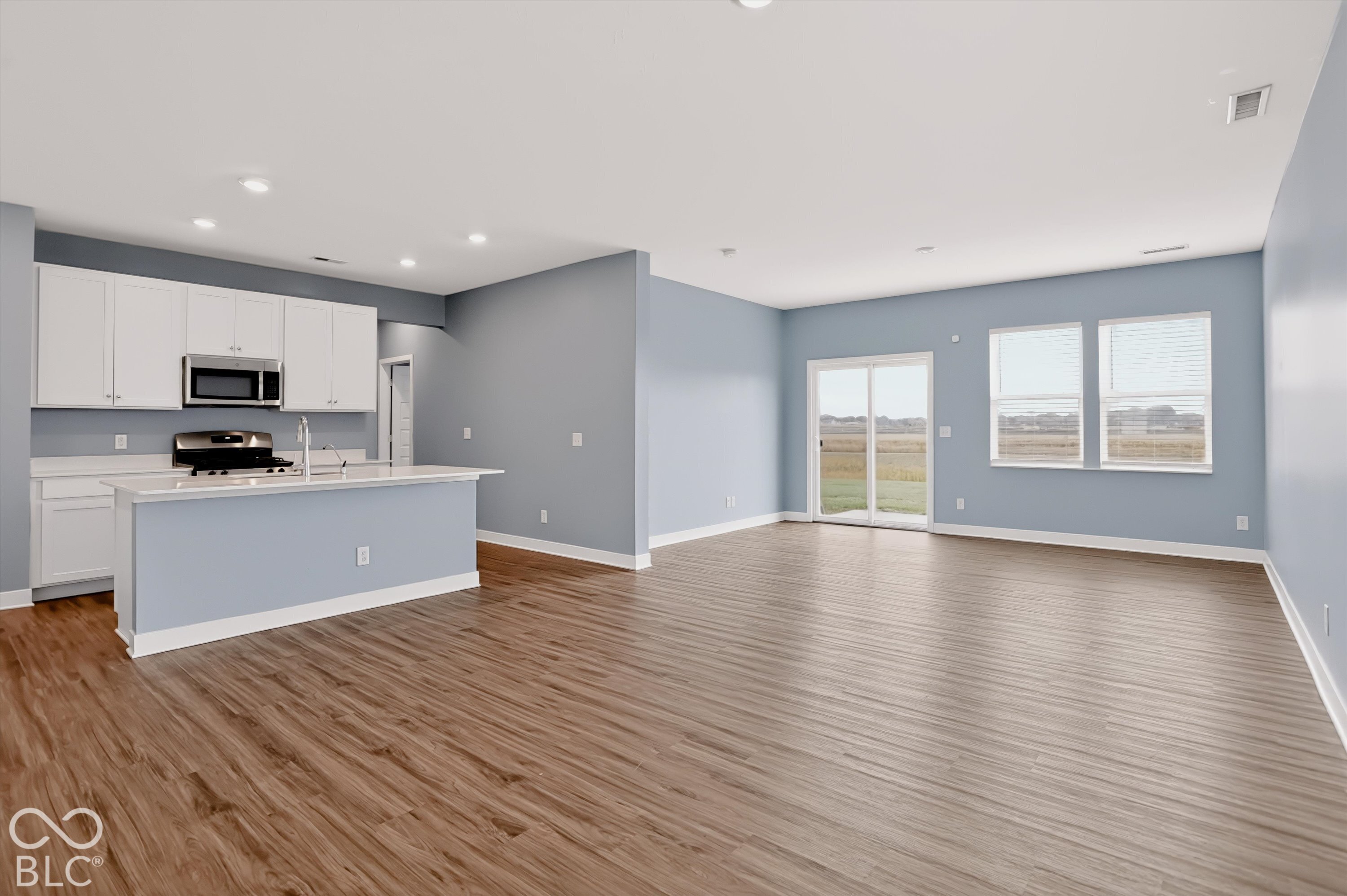 Open-concept area featuring wood-finish flooring, white cabinetry, a center island with a stone-surfaced countertop, recessed lighting, and a sliding glass door