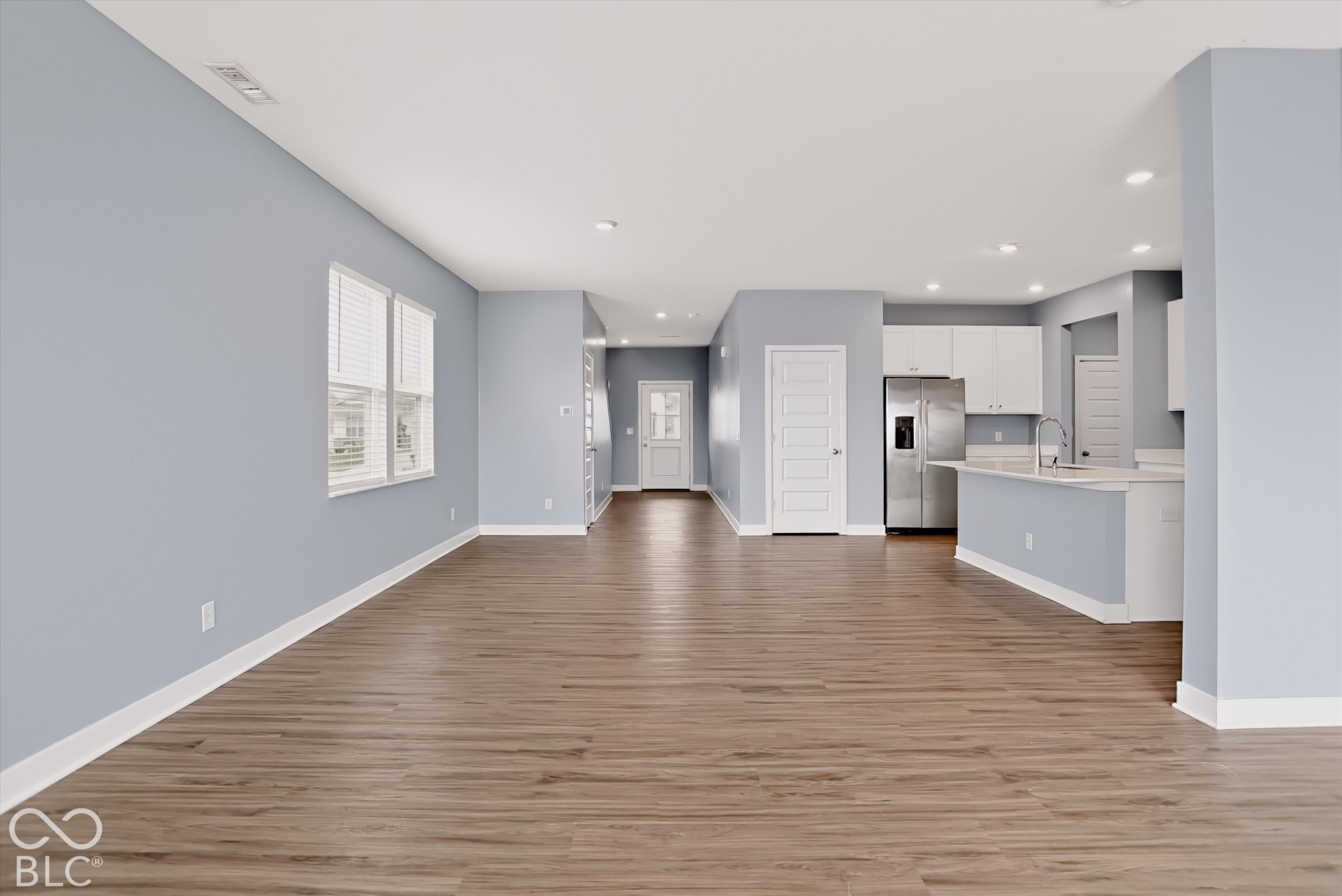Open-concept interior featuring wood-finish flooring, recessed lighting, and a kitchen equipped with white cabinetry and a breakfast bar