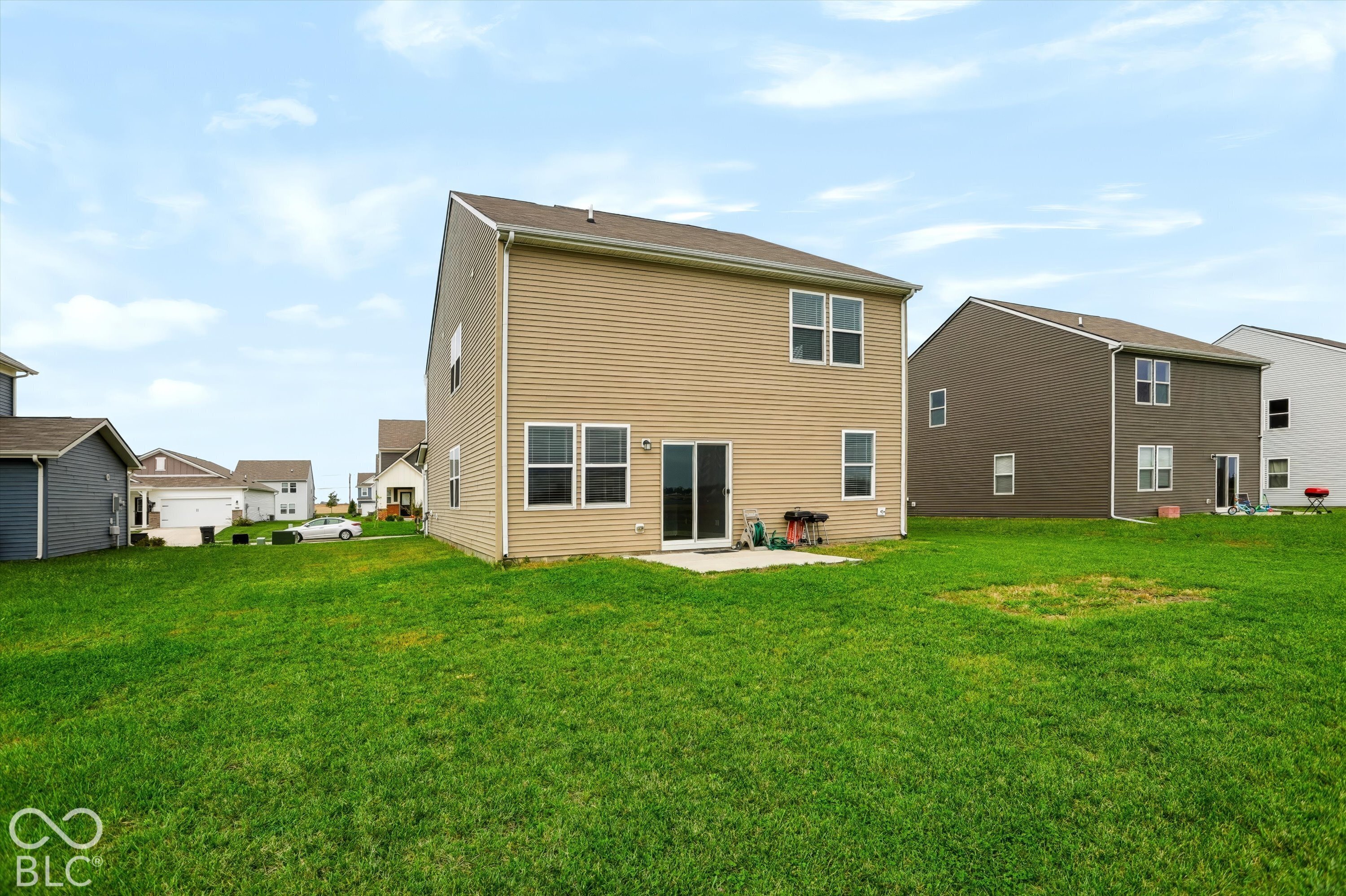 Two-story residence featuring light-toned horizontal siding, a concrete rear patio, sliding glass door, and a grass-covered backyard