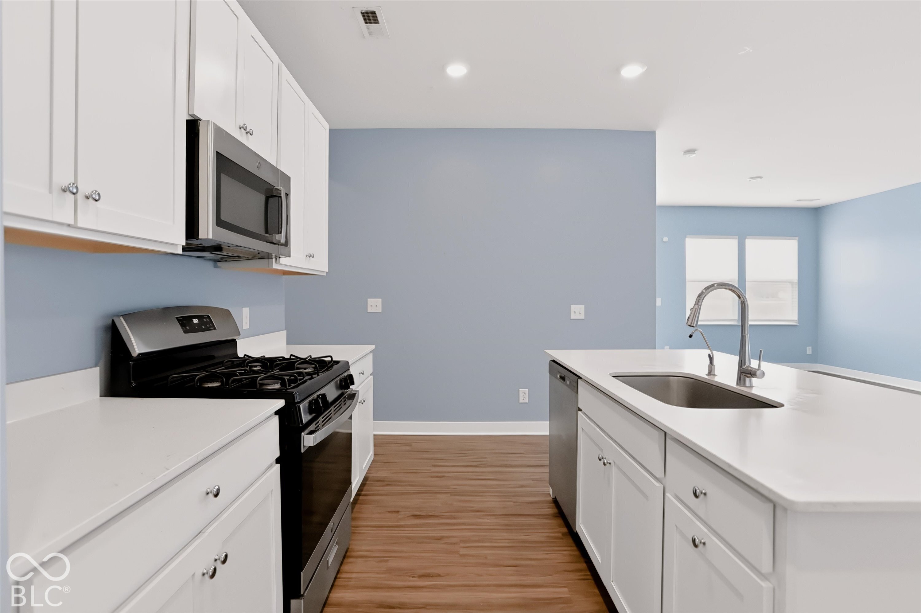 Kitchen featuring white cabinetry, solid-surface countertops, wood-finish flooring, stainless steel appliances, and a center island with a stainless steel sink