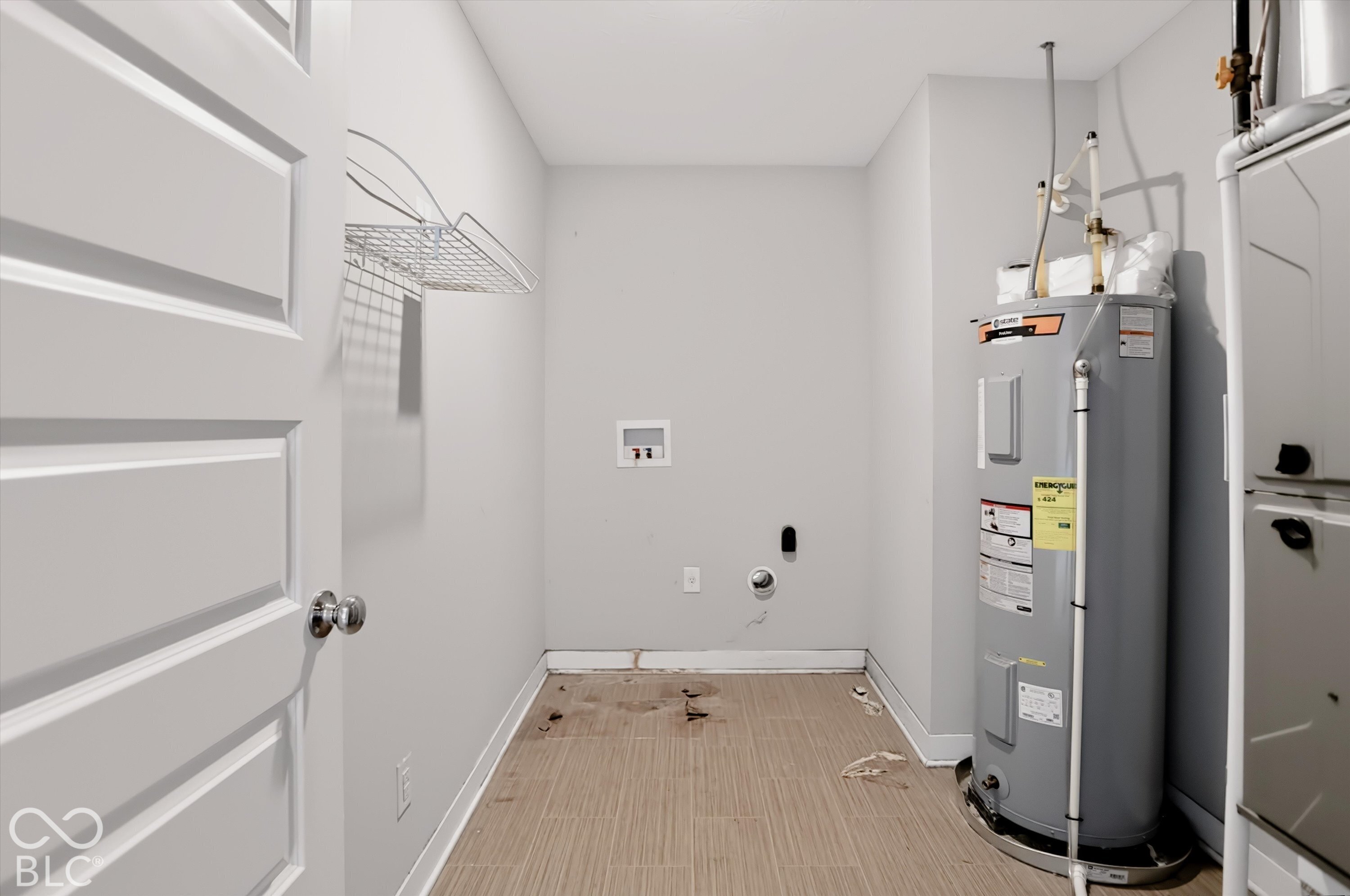 Utility area featuring a wall-mounted wire storage shelf, dedicated washer and dryer hookups, tile flooring, and an integrated water heater