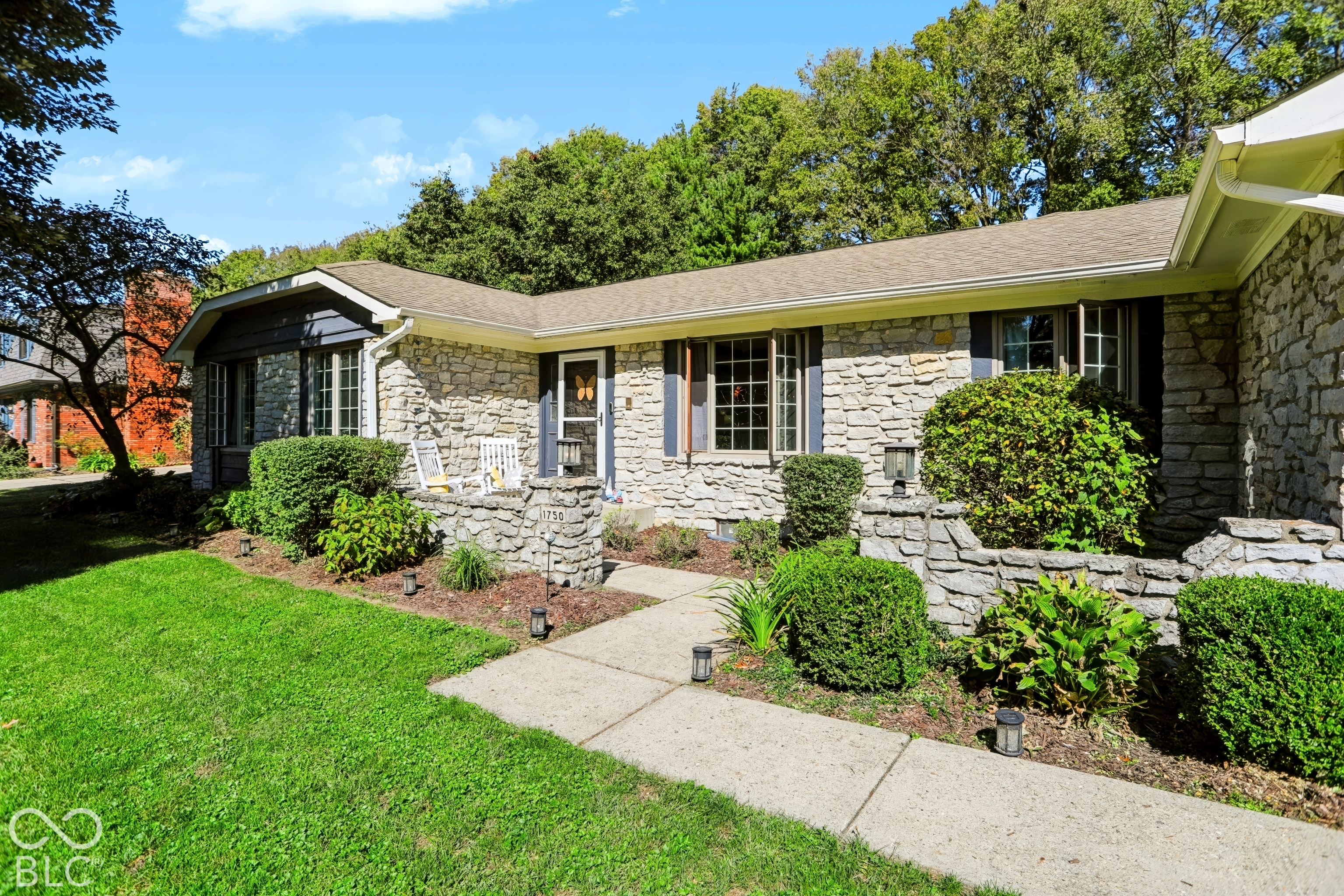 Stone veneer exterior with dark shutters, gabled roofline, and landscaped front yard