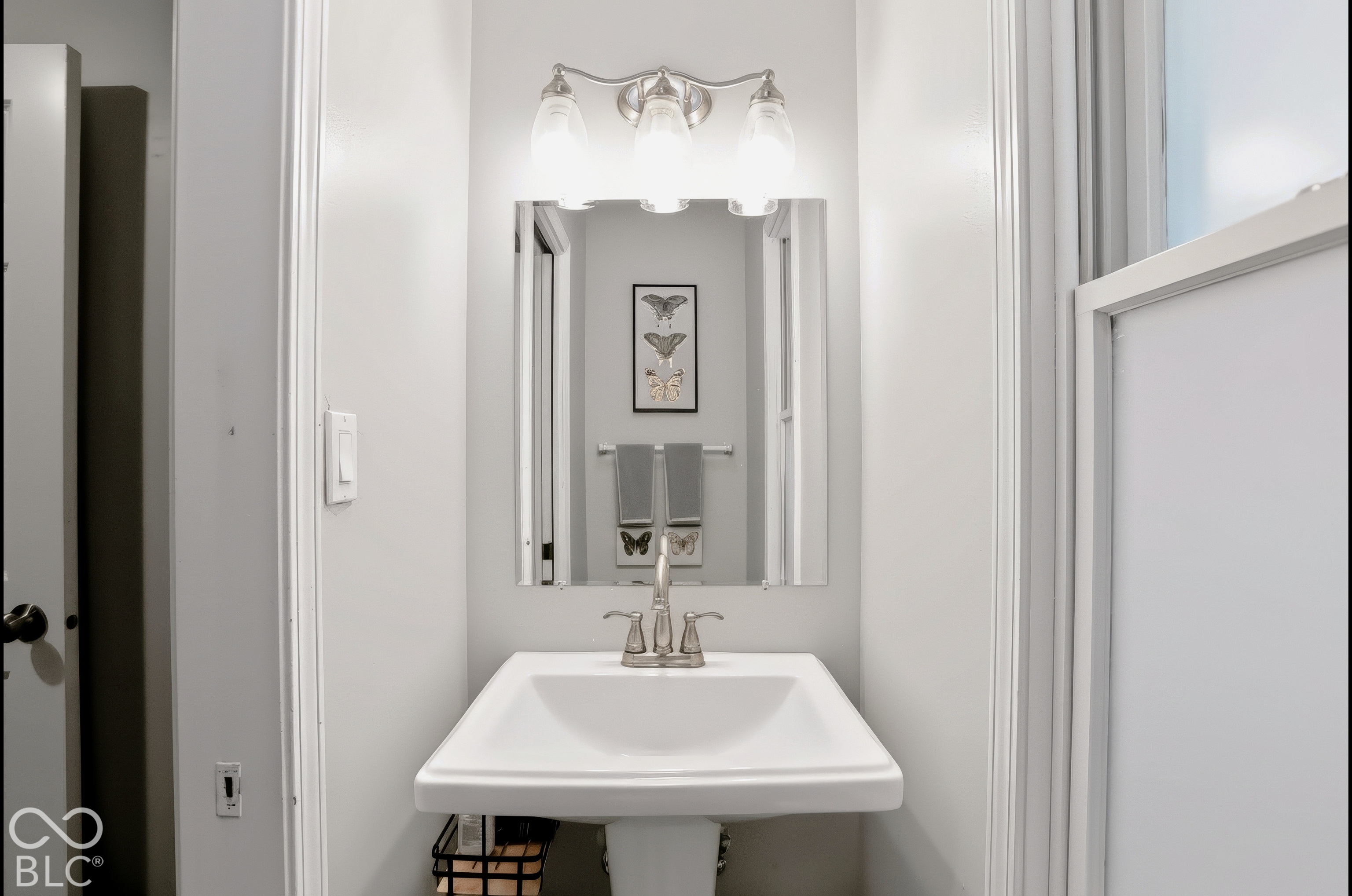 Pedestal sink with a brushed nickel faucet, mirror, and a three-light vanity fixture
