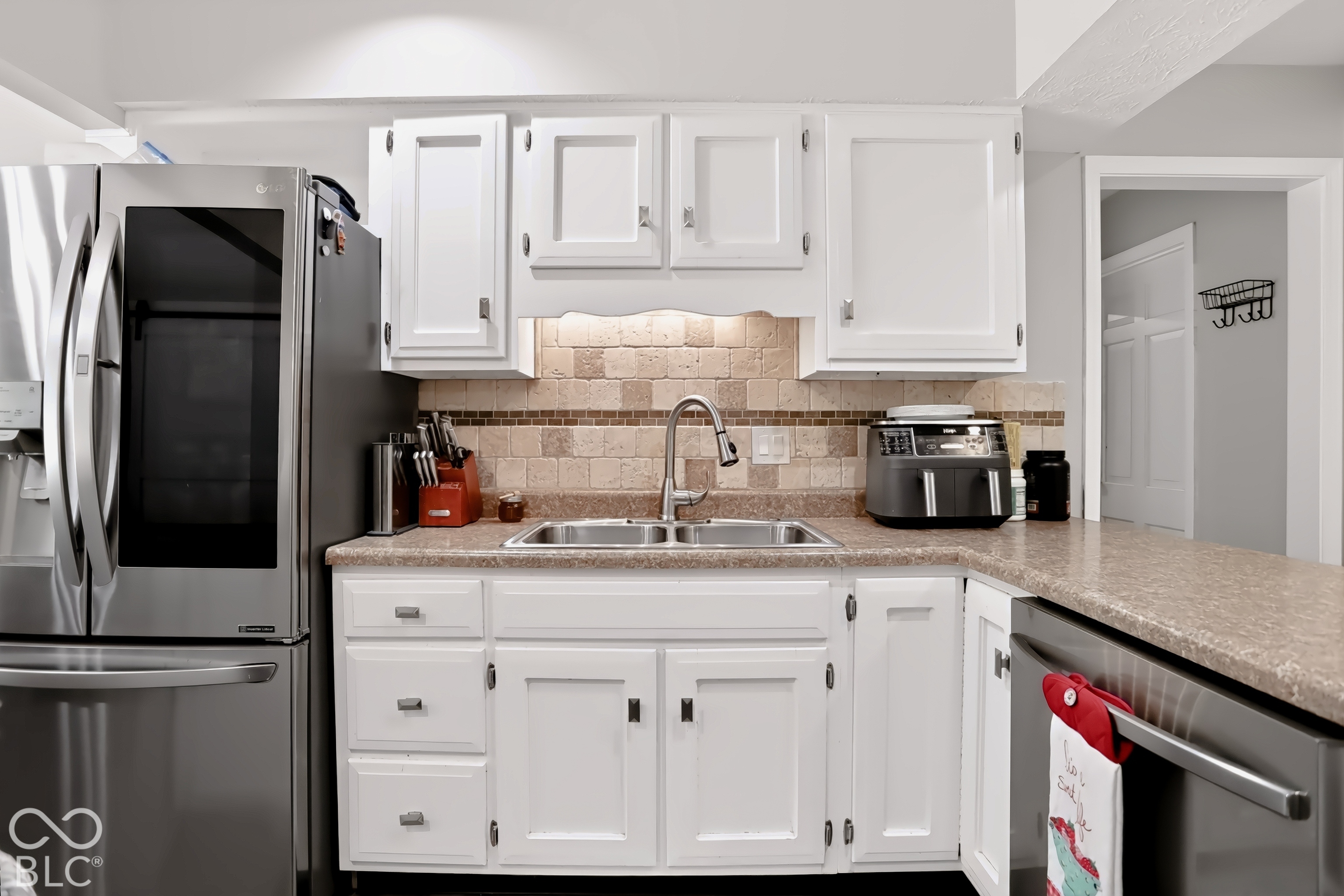 White cabinetry with brushed nickel hardware, stainless steel appliances, a double basin sink with a high-arc faucet, and a stone-finish tile backsplash