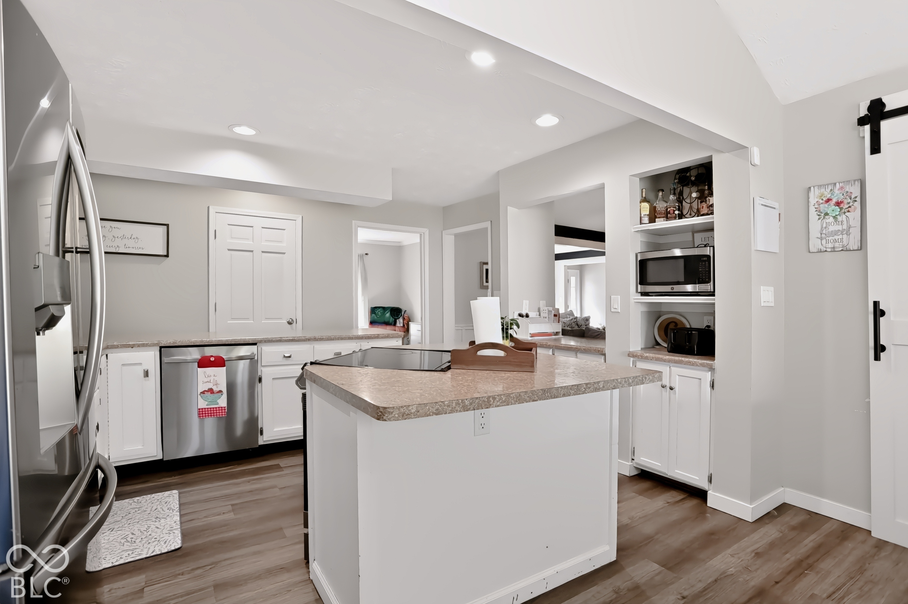 Kitchen featuring an island with a countertop, stainless steel refrigerator, stainless steel dishwasher, built-in shelving, and wood-finish flooring