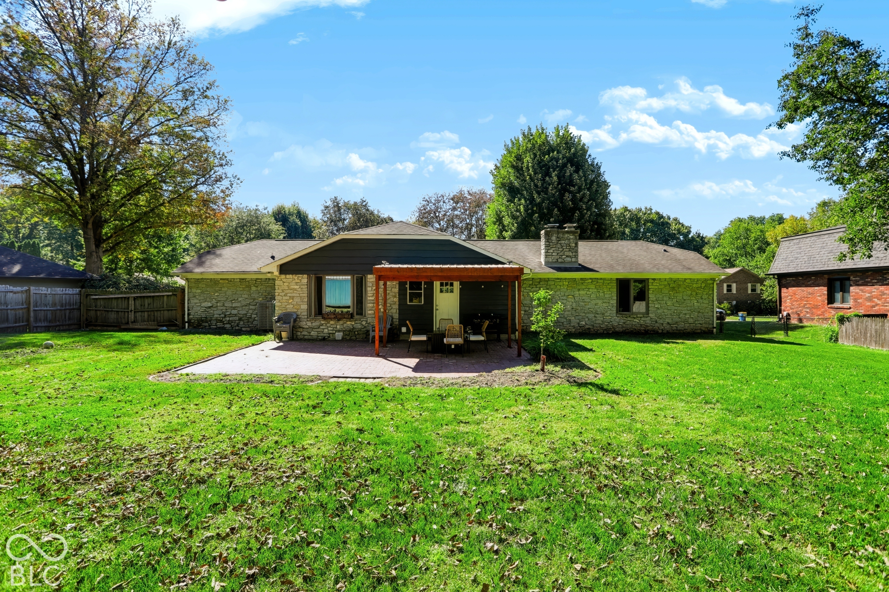 Expansive grassy yard with a stone-clad exterior, covered patio, brick chimney, and mature trees