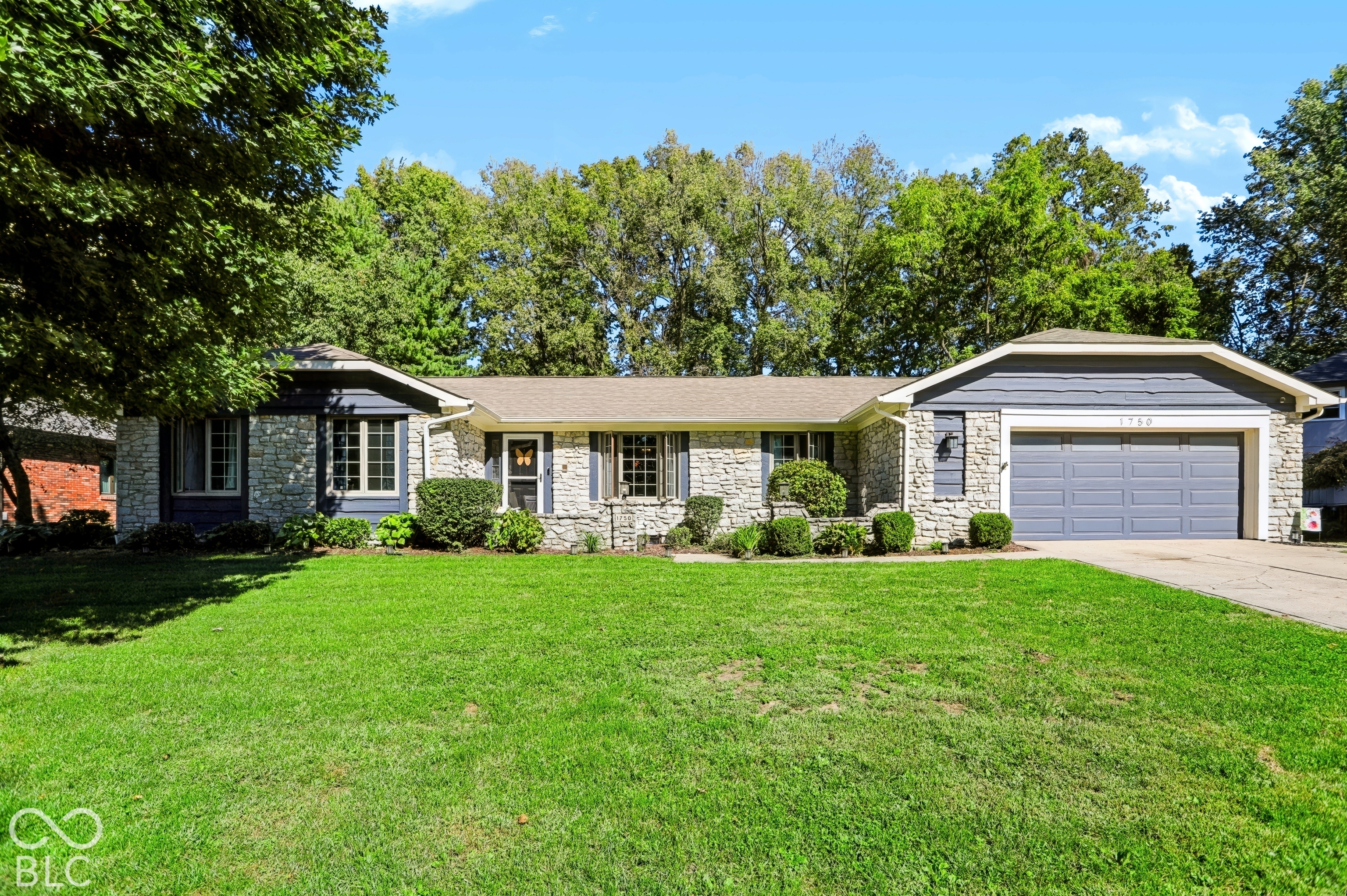 Stone facade residence with a two-car garage, mature landscaping, and a well-maintained lawn Stone facade residence with a two-car garage, mature landscaping, and a well-maintained lawn