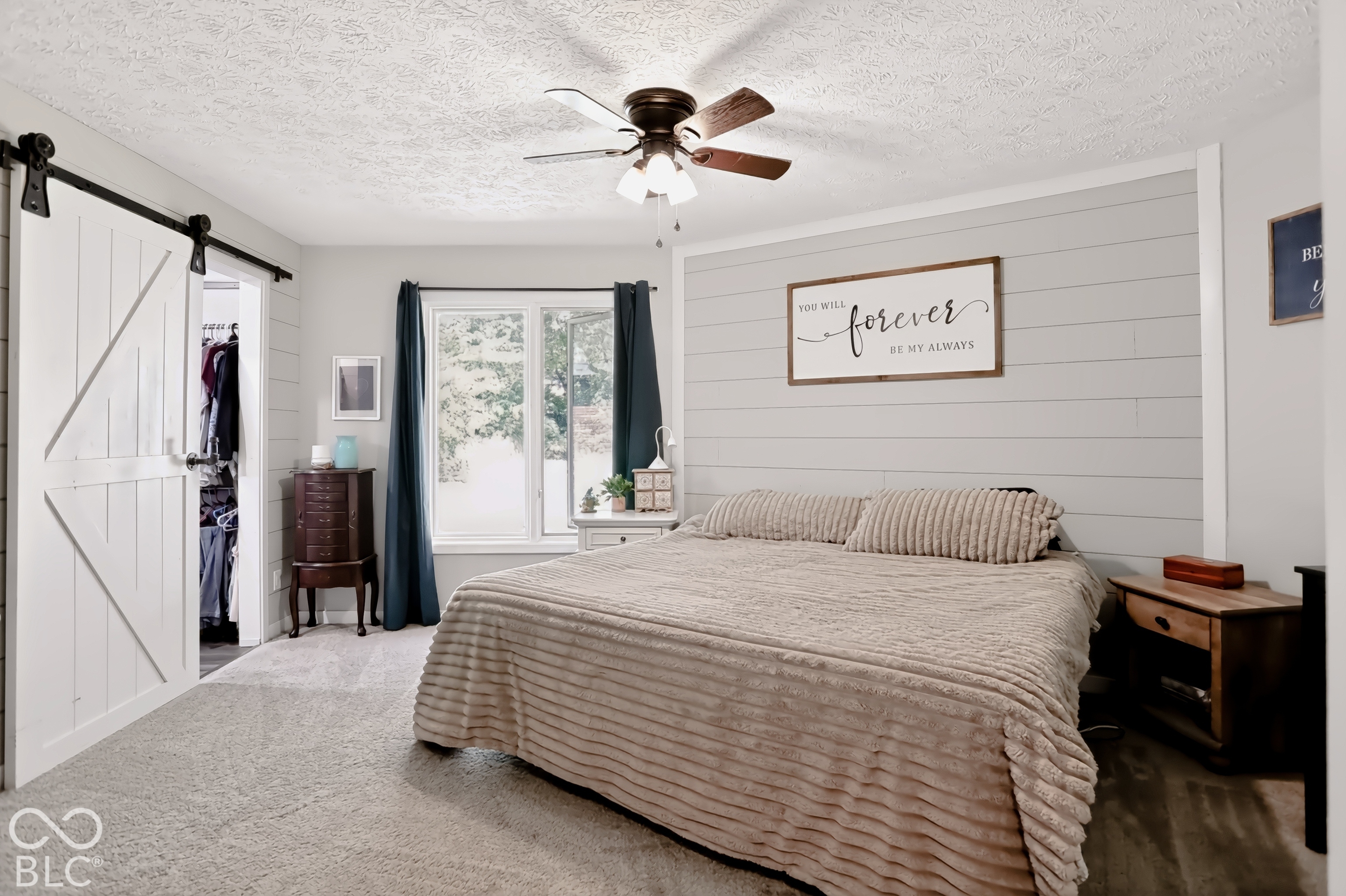 Ceiling fan with integrated lighting, window with white trim, gray shiplap accent wall, white barn door on a black track, and carpeted flooring